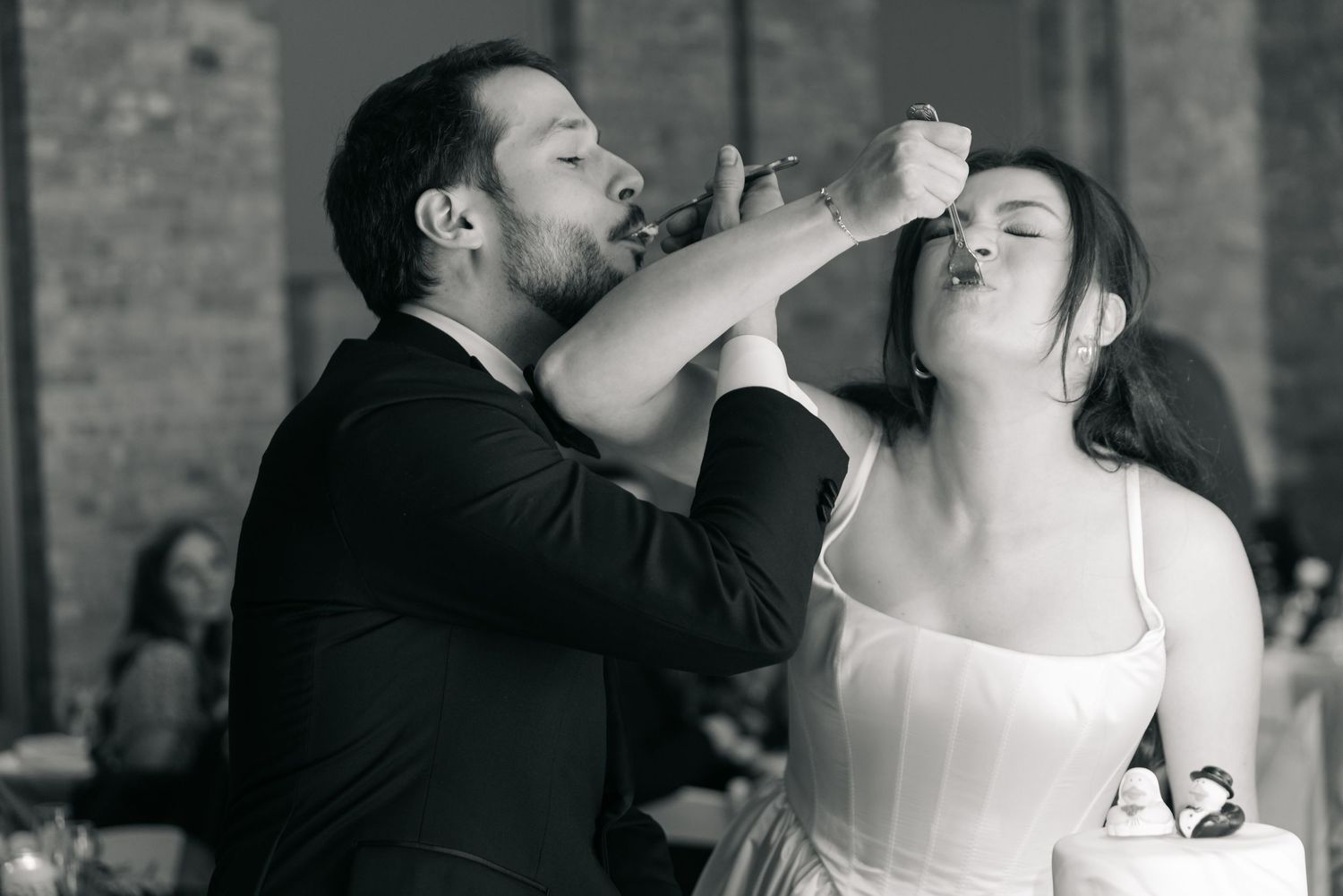 Black and white photo of bride and groom feeding each other wedding cake at their reception.