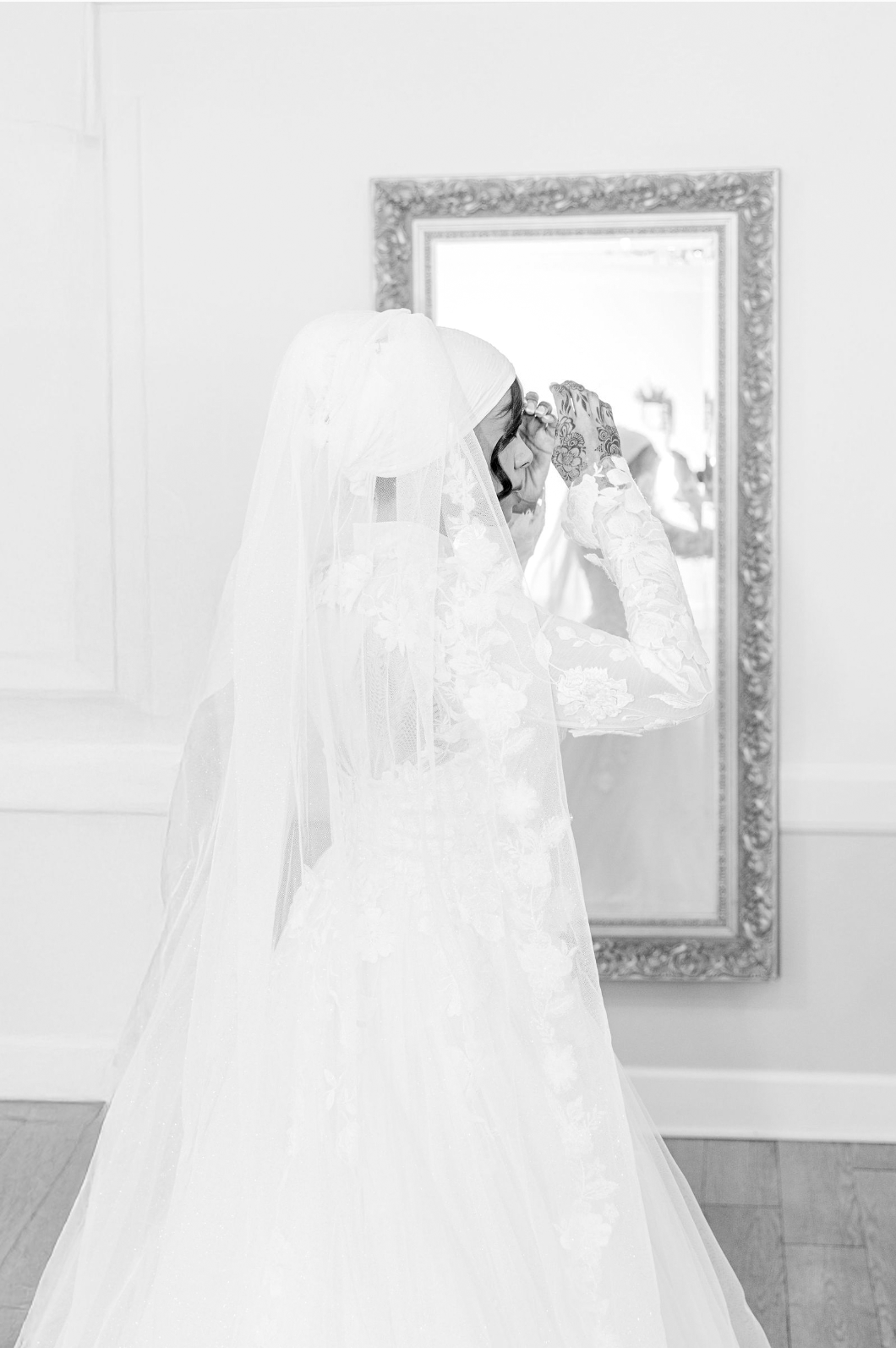 A wedding dress and veil on display in a bright white room with framed artwork on the wall.