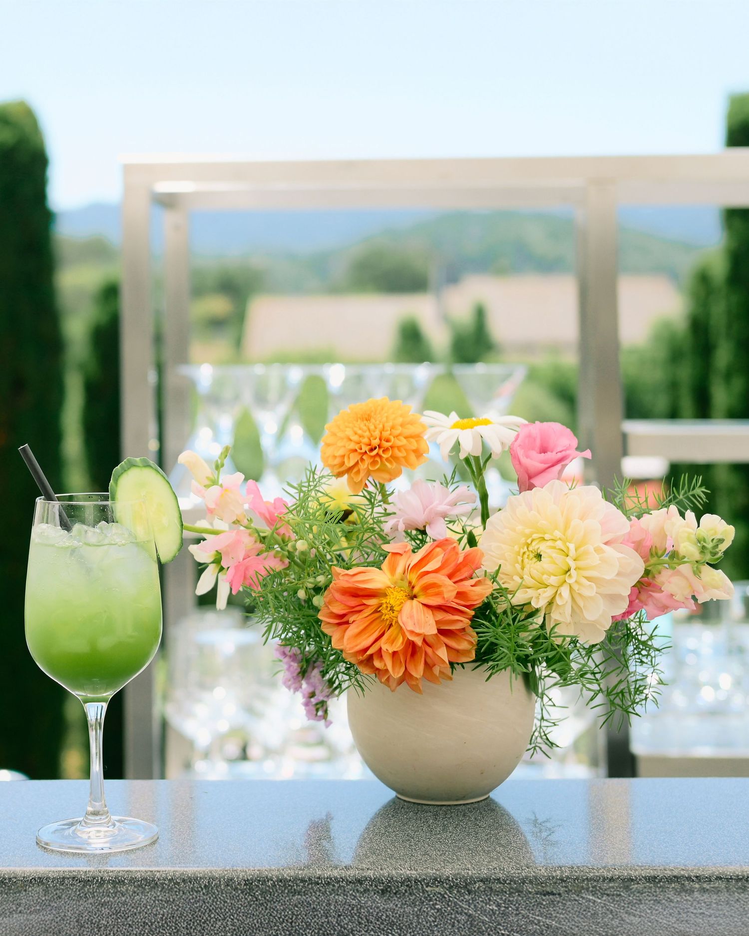Colorful floral centerpieces with orange and pink dahlias in beige vases alongside cocktail glasses.
