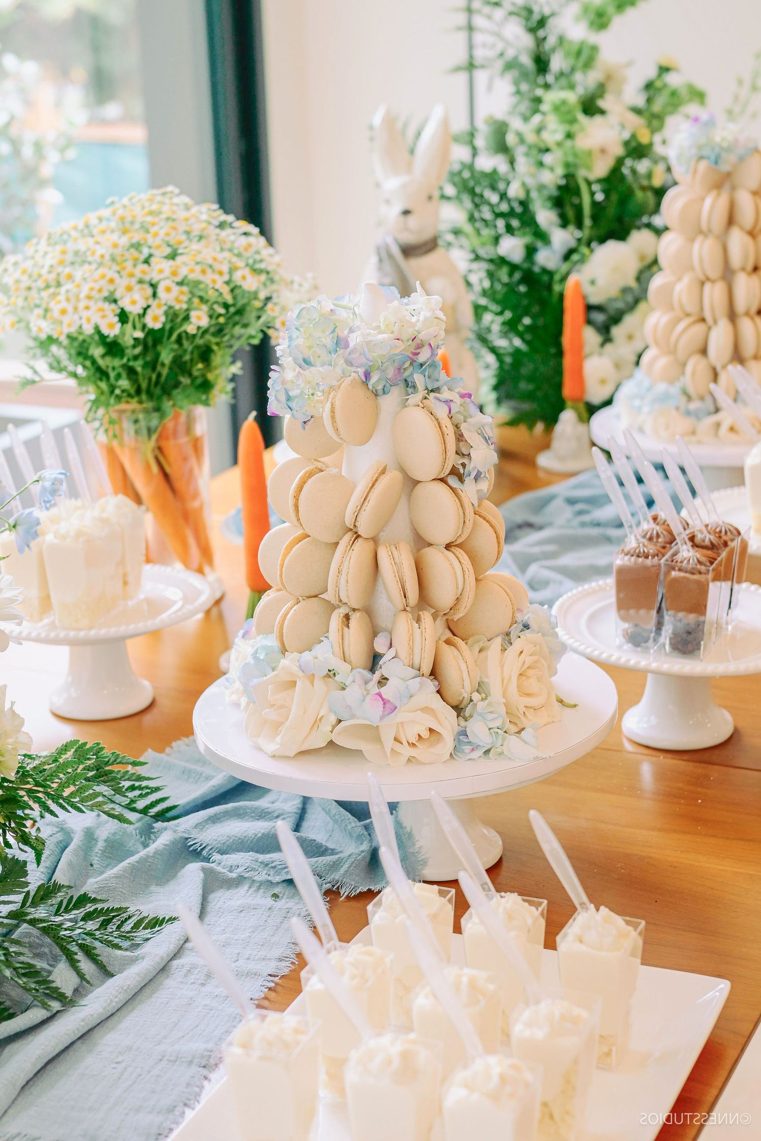 White macaron tower display with floral decorations and delicate pastries at an elegant event.