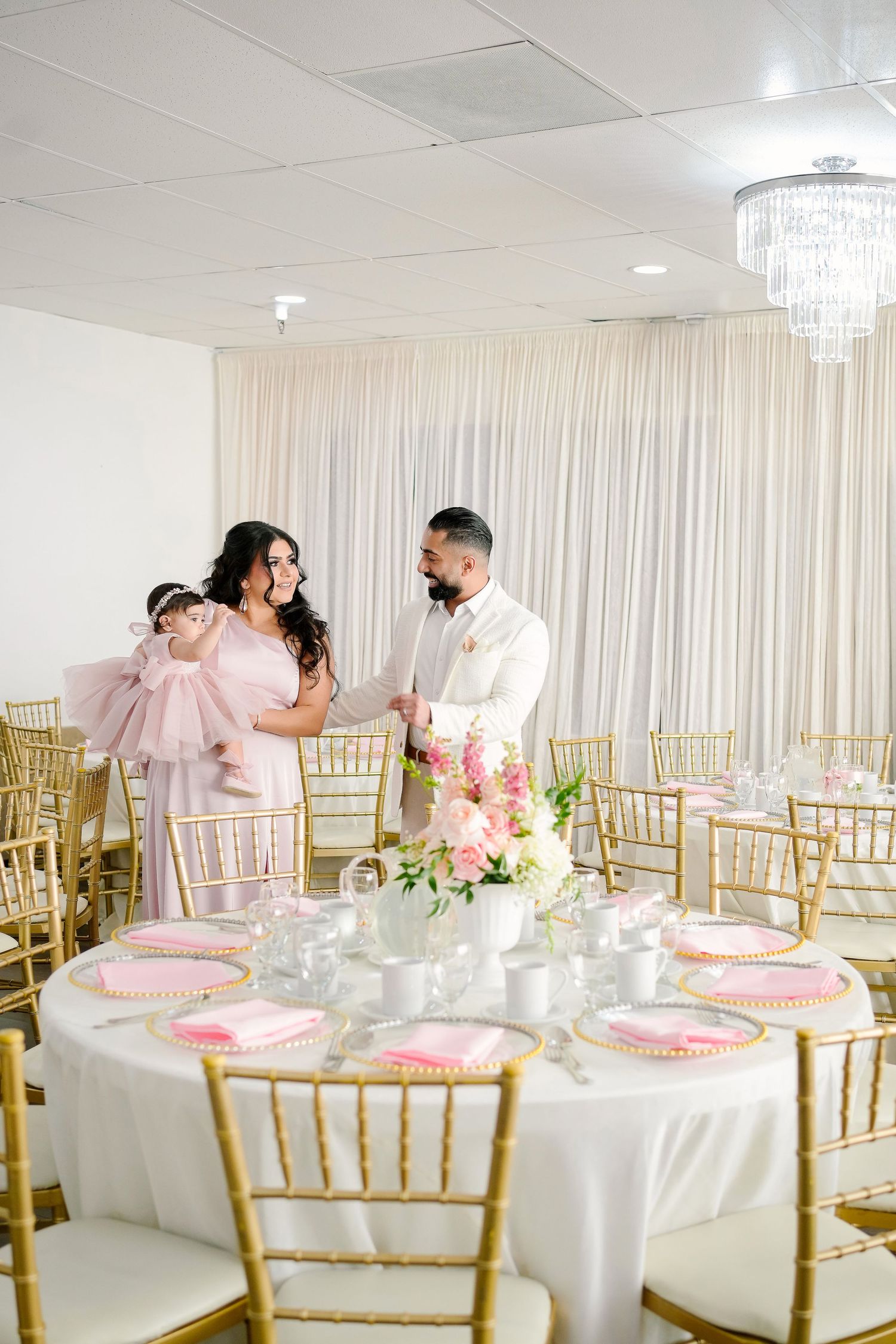 Elegant reception setup with gold chiavari chairs and white tablecloths in a bright banquet room.