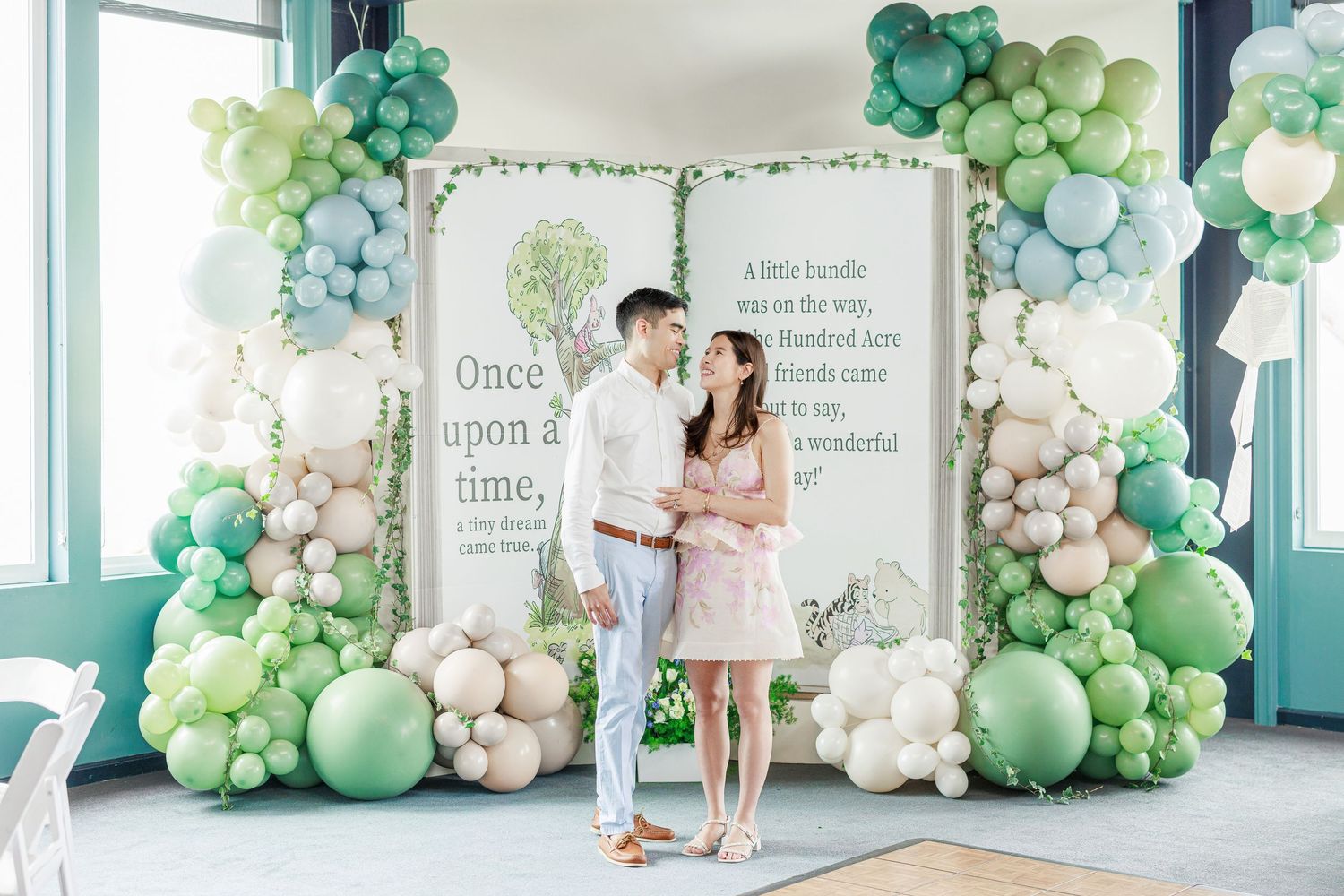 Whimsical balloon arch installation in soft green and white colors decorating an indoor space with fairy tale signage.