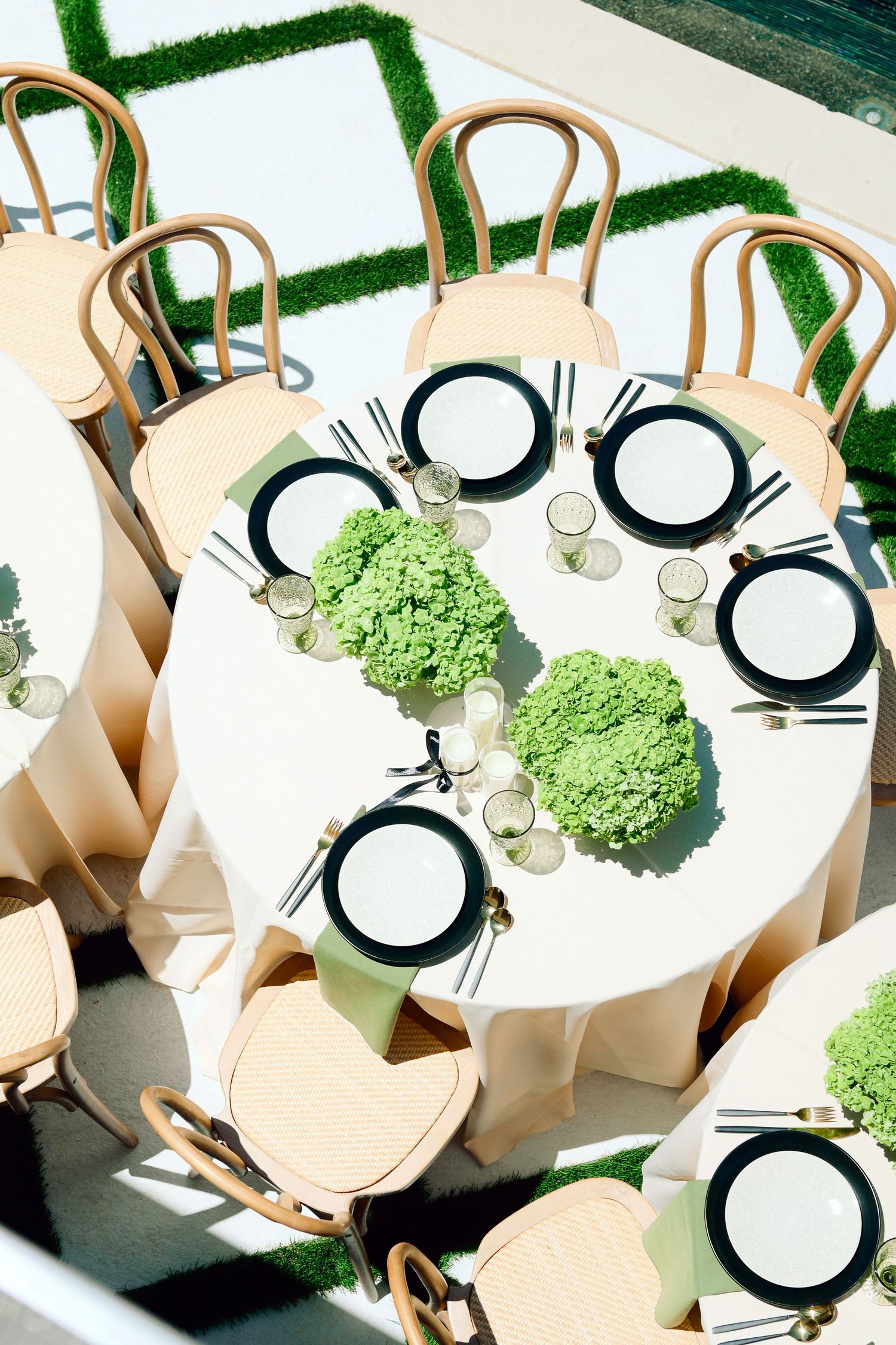 Modern table settings with white plates and green hydrangea centerpieces on round tables.