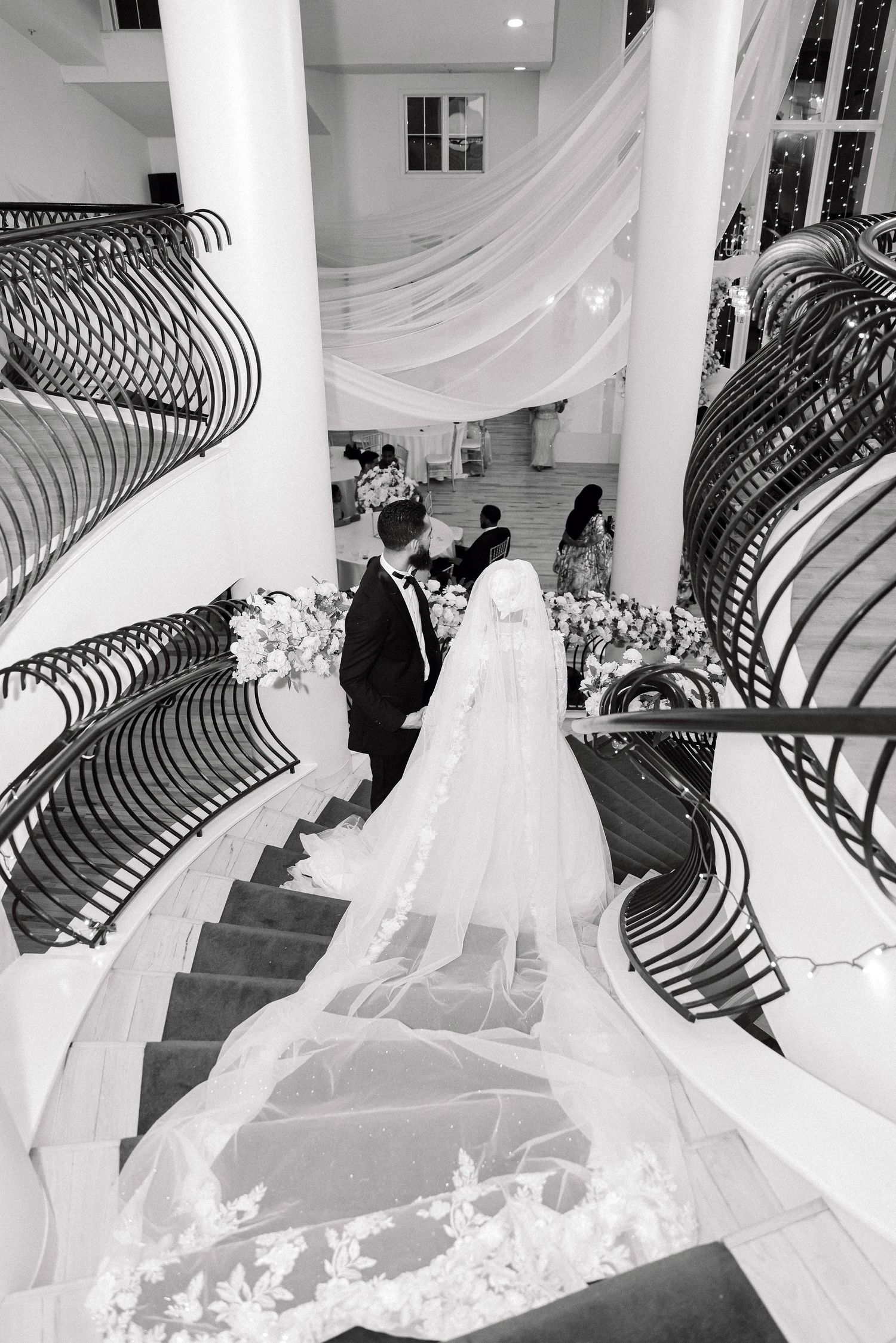 Wedding couple descending elegant curved staircase with long flowing veil.