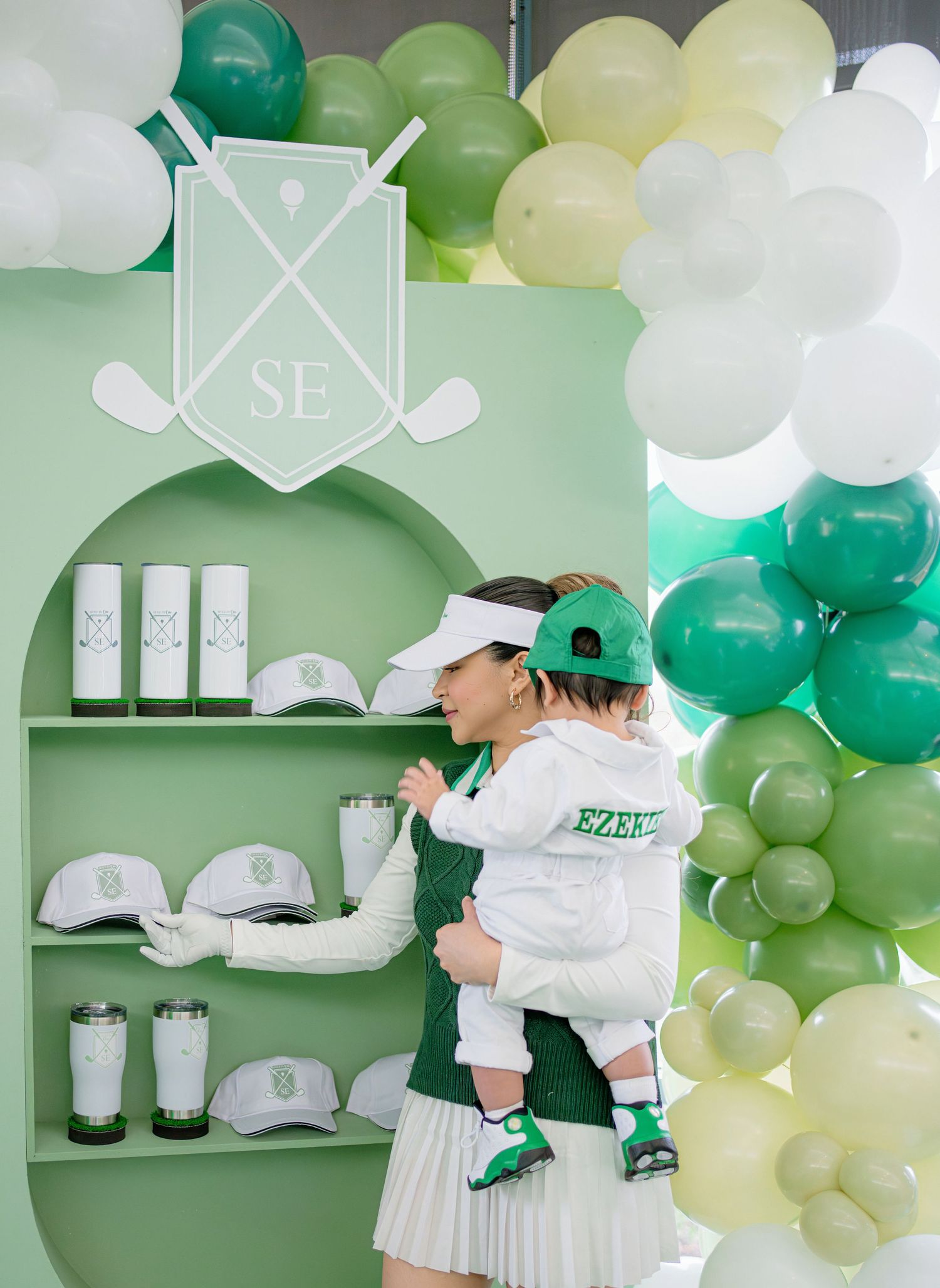 A green and white themed party display with balloons, cups, and decorative shelving showcases a sporty aesthetic.