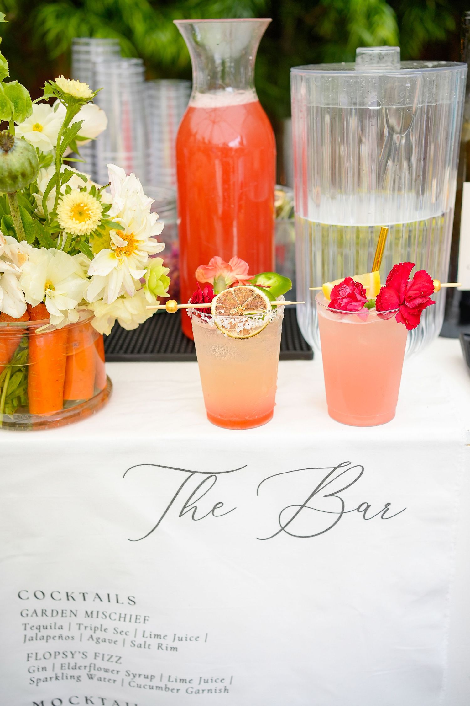 Close-up of cocktail menu and drinks display with elegant calligraphy signage and coral-colored beverages.