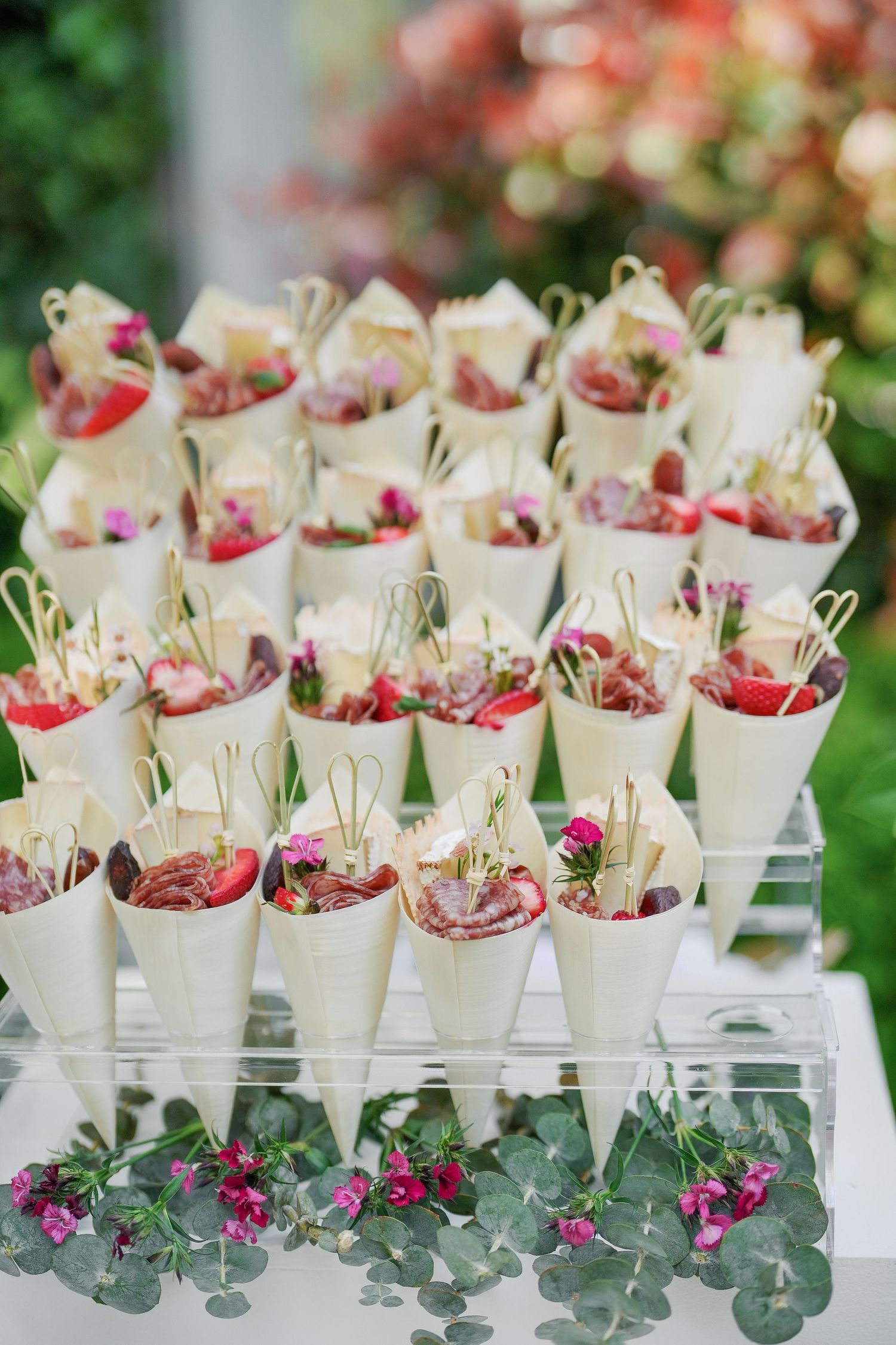 White paper cone appetizers decorated with flowers and arranged on eucalyptus leaves.