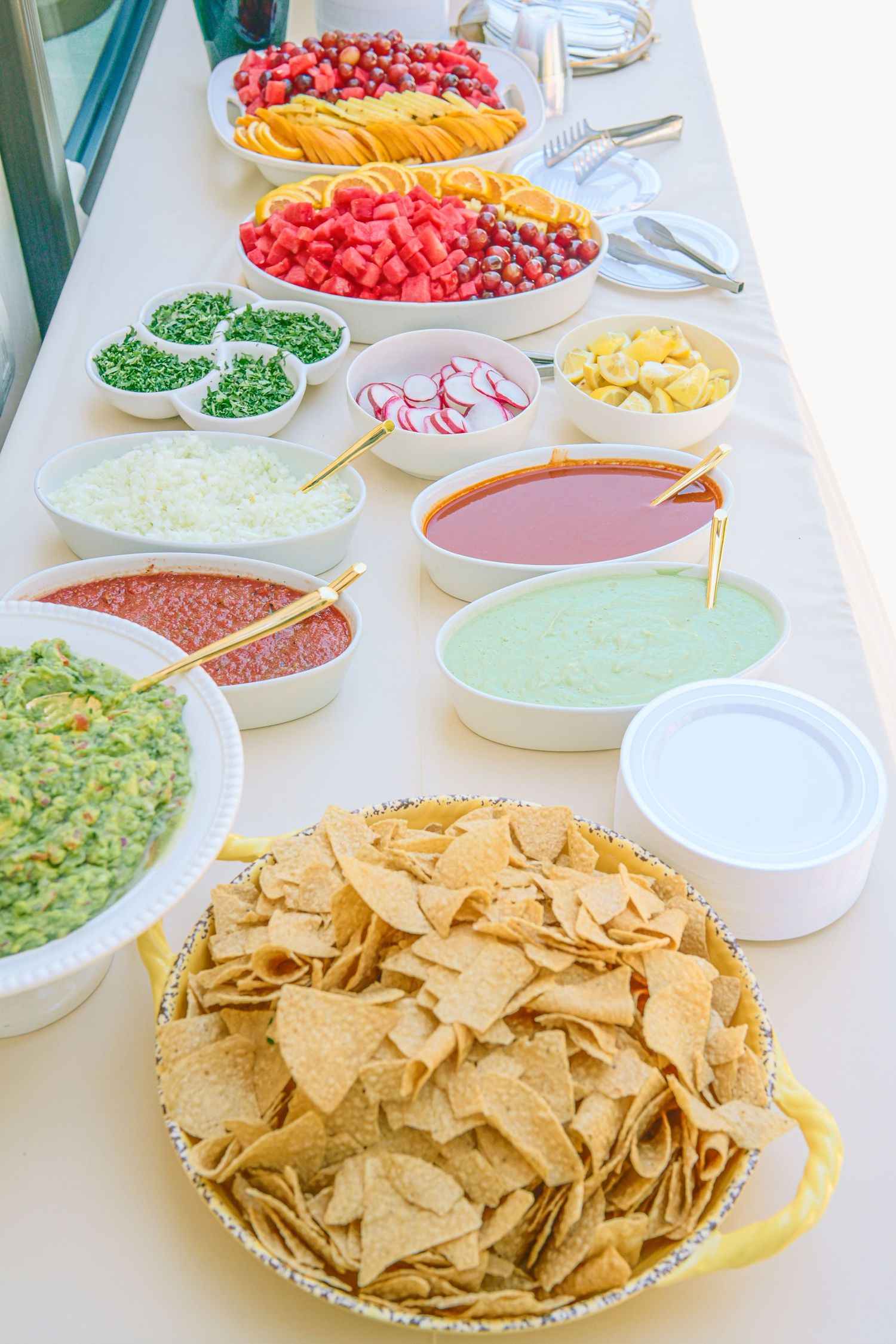 Colorful party buffet spread with chips, dips, and fresh fruit platters.