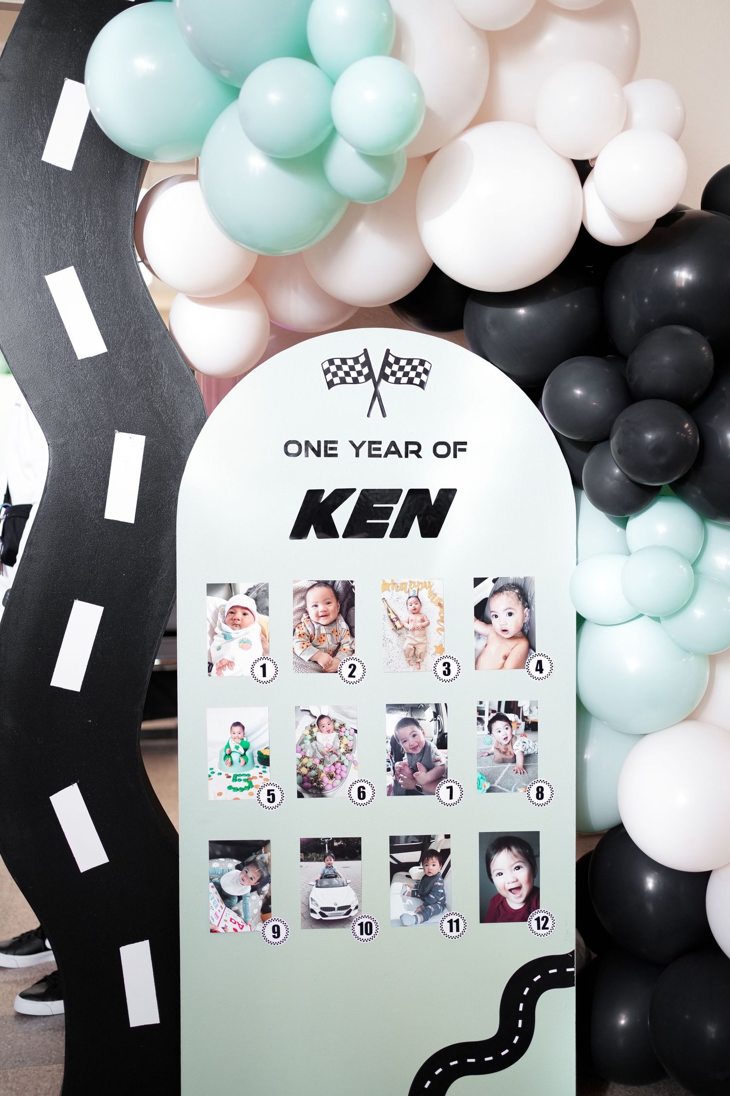 Racing themed first birthday party display with balloon garland in mint, white and black colors featuring photo collage board.