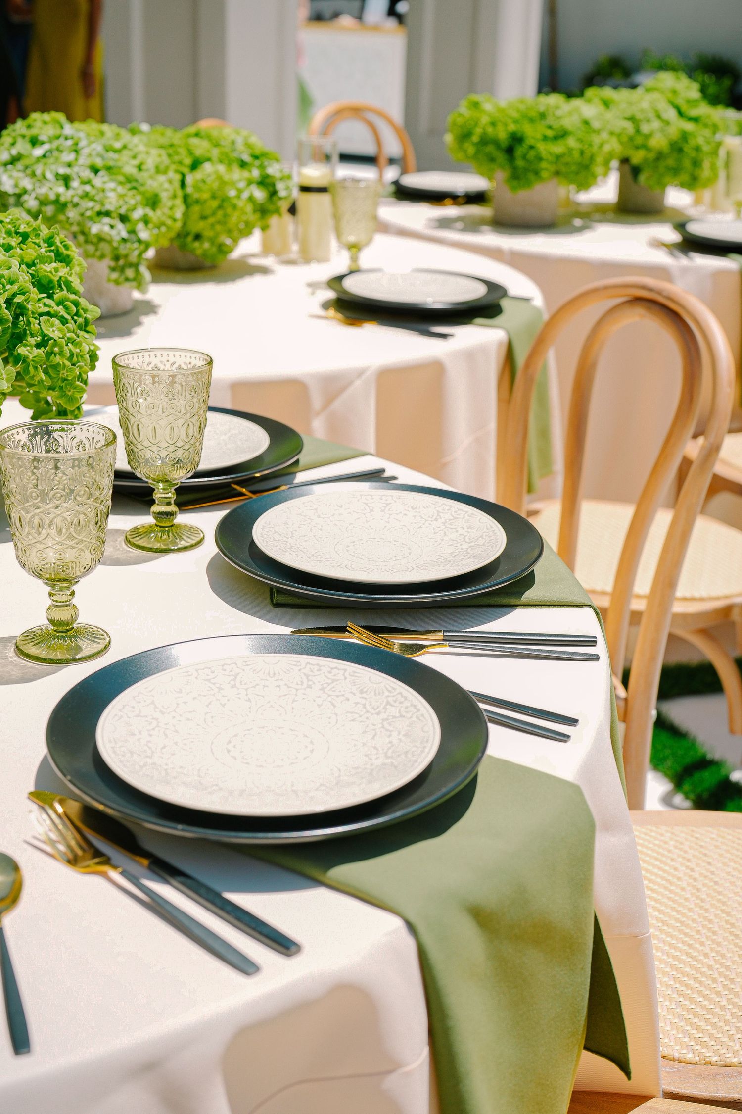 Minimalist place settings with black charger plates and green napkins on white tablecloths.