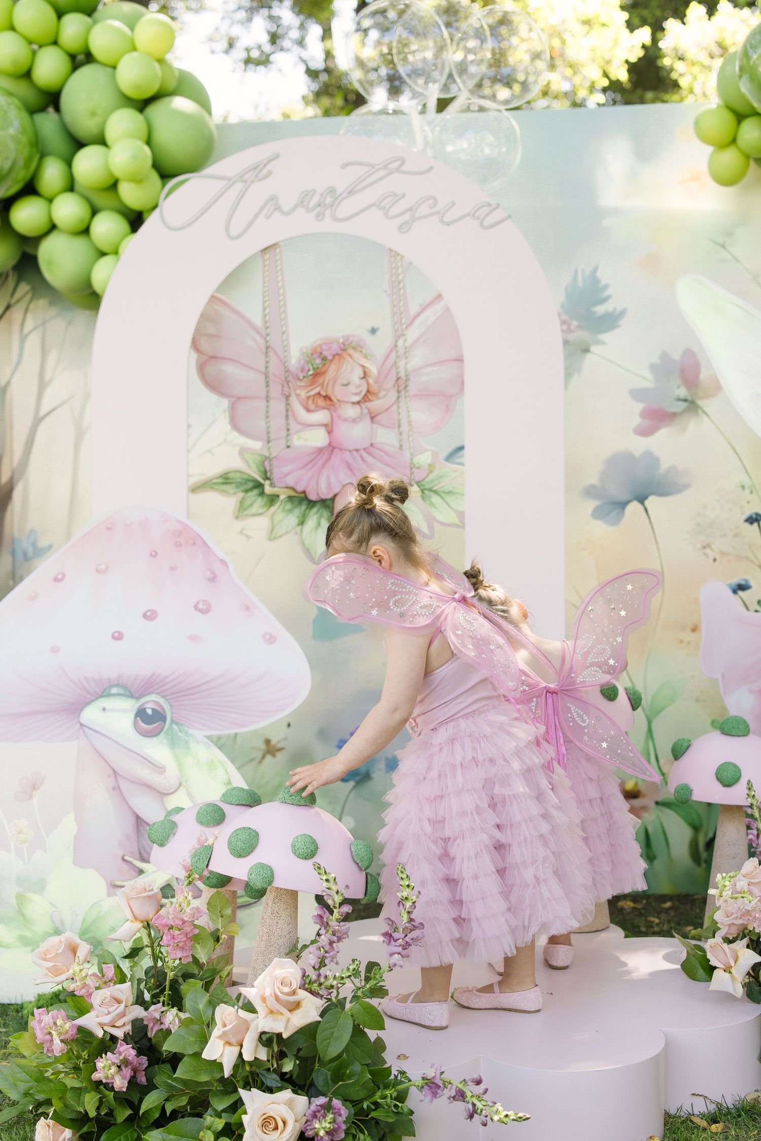 Enchanted fairy garden setup with pink tulle dresses and green balloon arrangements.