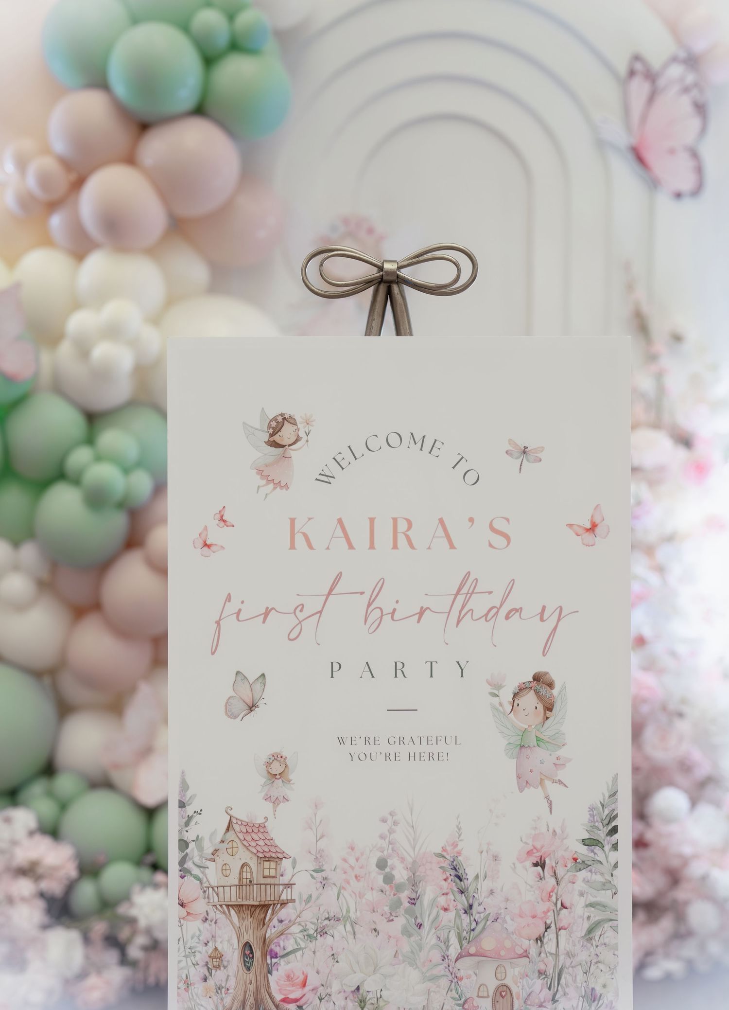Elegant first birthday welcome sign with pastel balloon arch and fairy garden theme featuring butterflies and delicate artwork.