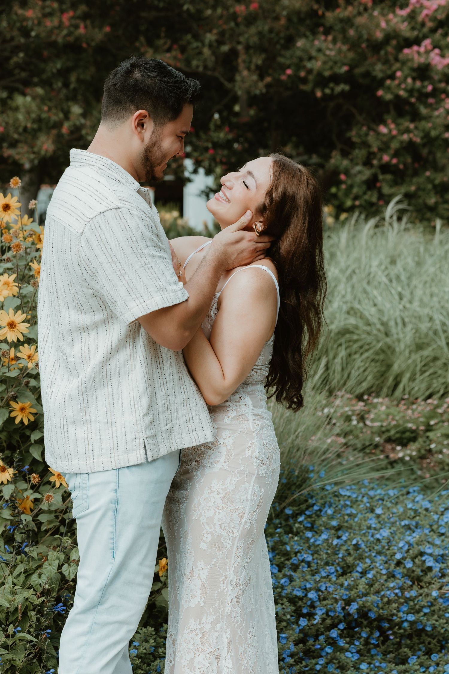 A romantic couple embraces in a garden setting with blue flowers and greenery in the background.