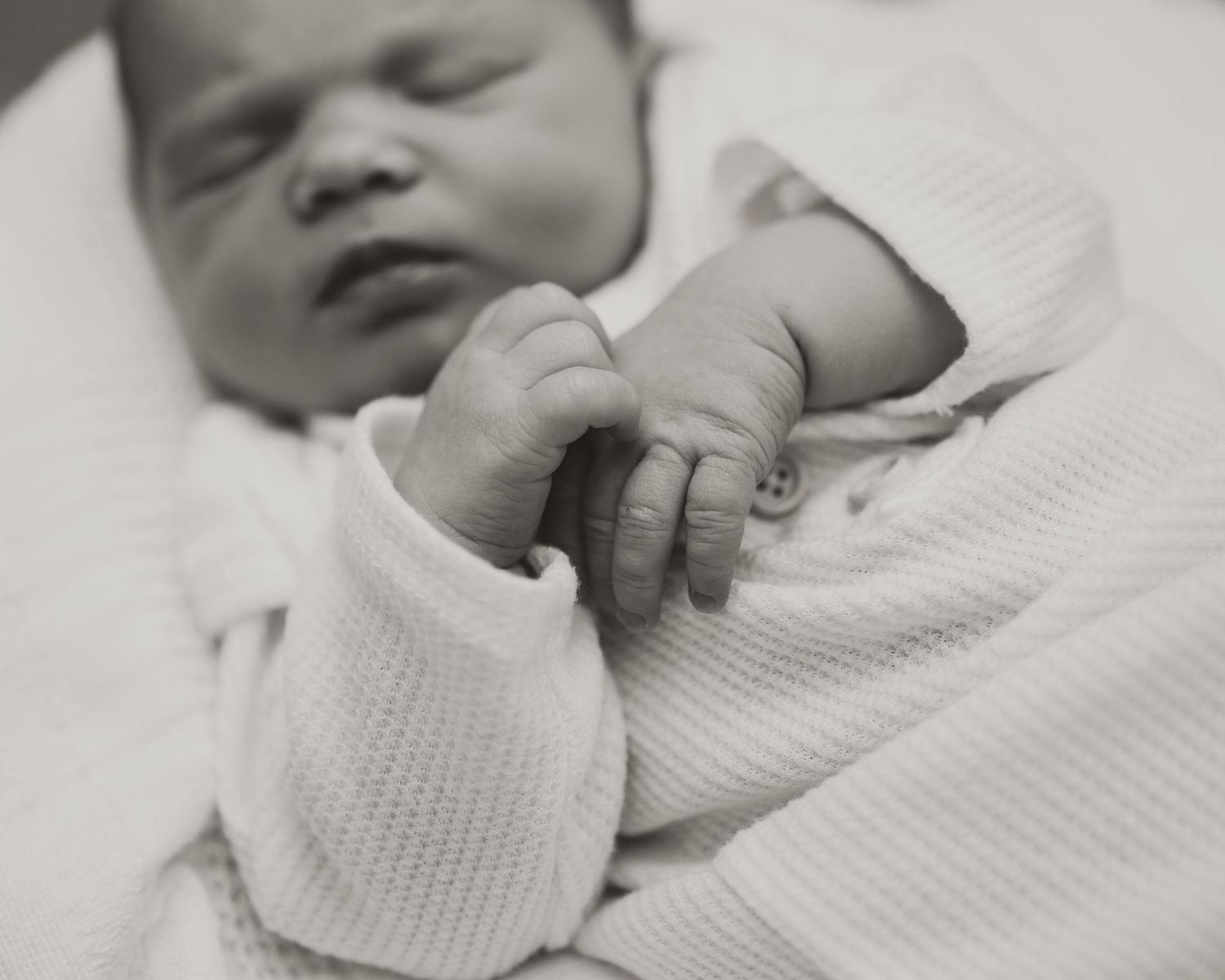 A series of black and white photographs showing a sleeping newborn baby wrapped in a white textured blanket.