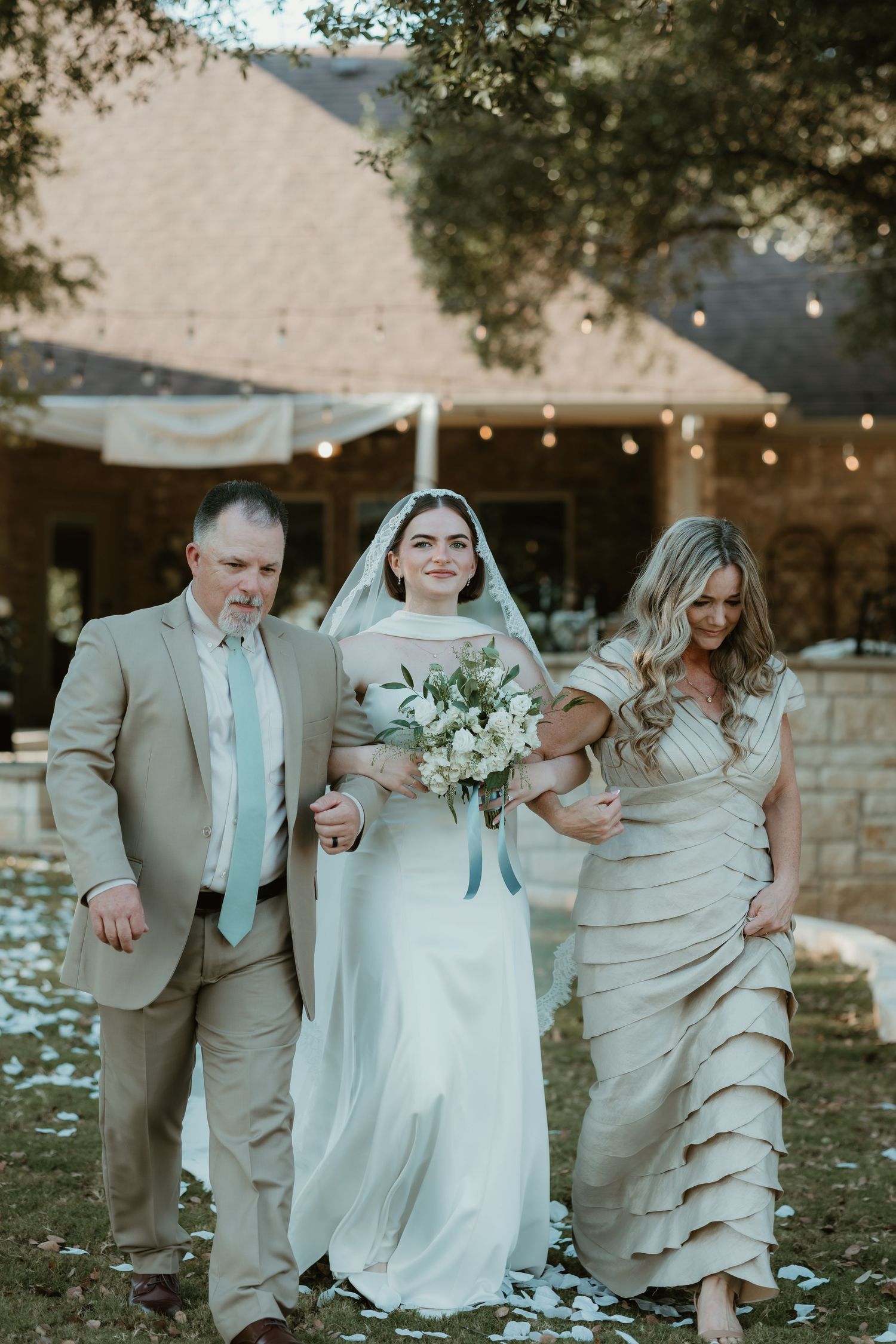 Wedding party walking together outdoors with confetti falling while wearing beige and white formal attire.