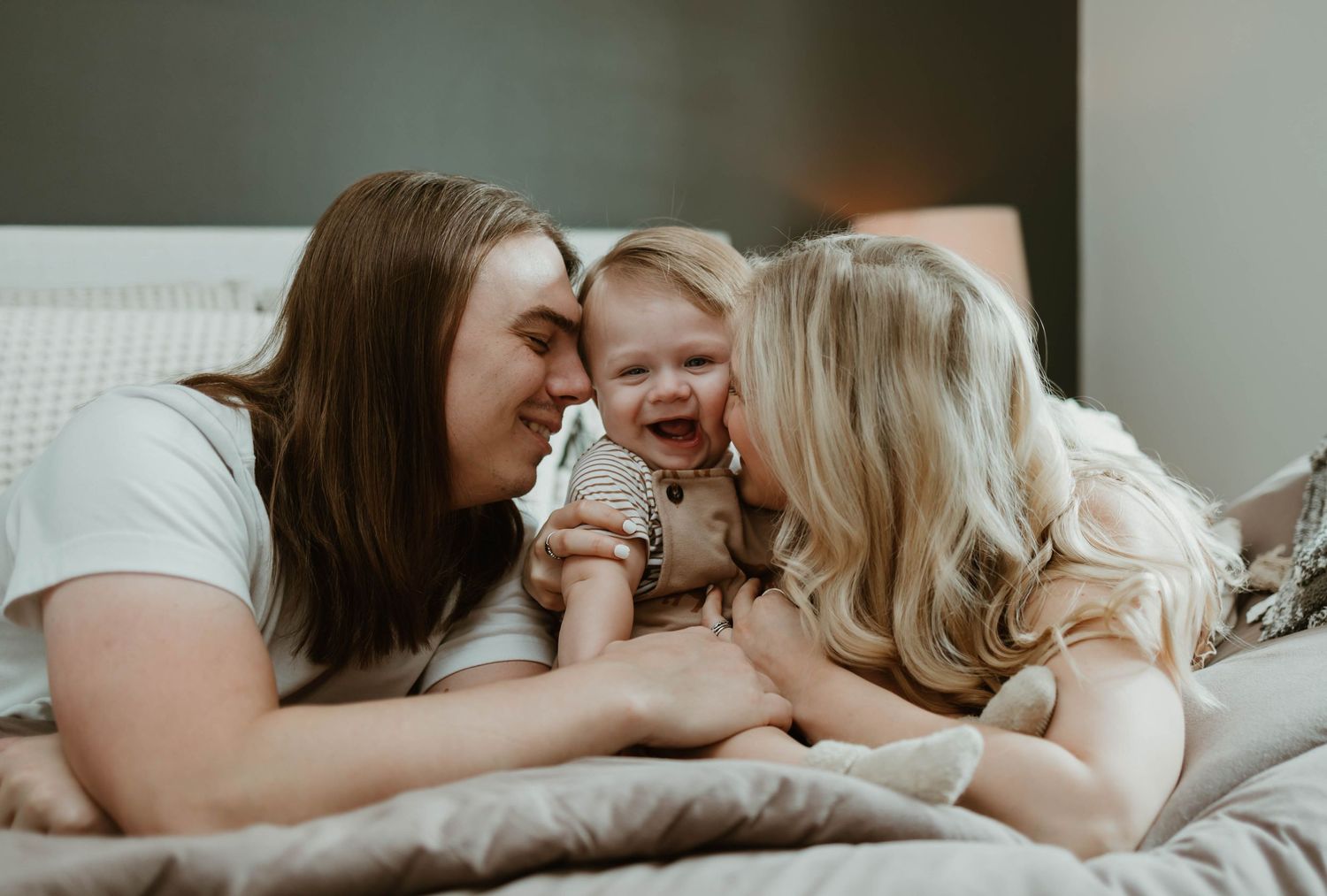 Family members share tender moments while lying together on a cozy bed in soft natural light.