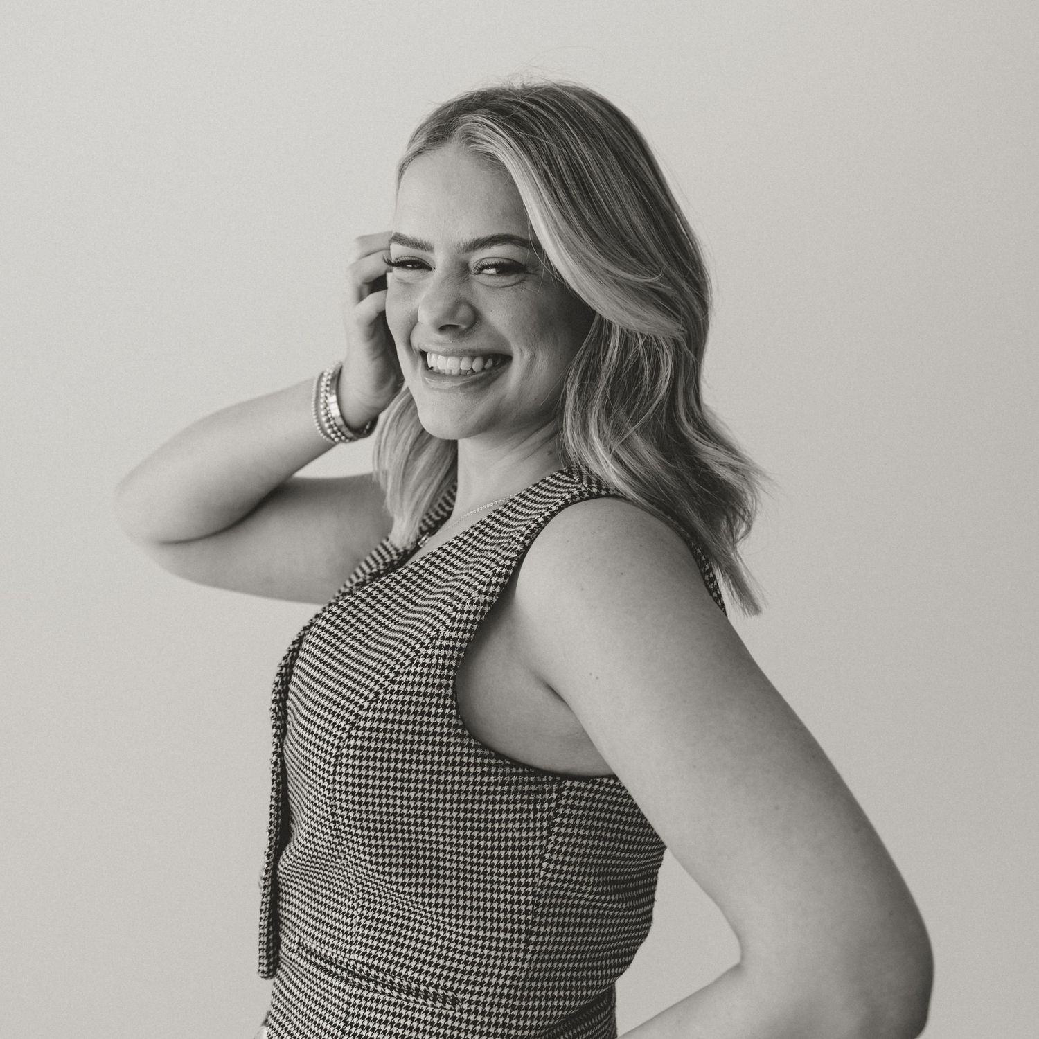 Black and white portrait of a smiling woman in a checkered sleeveless top posing against light background.