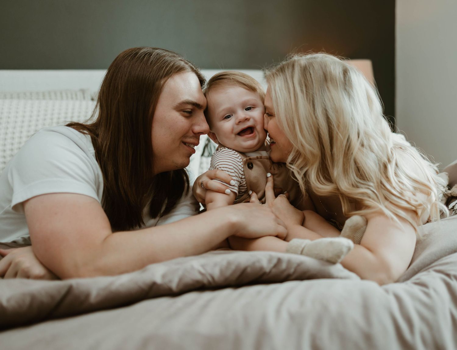 A loving family cuddles together in bed while sharing tender moments in soft natural light.
