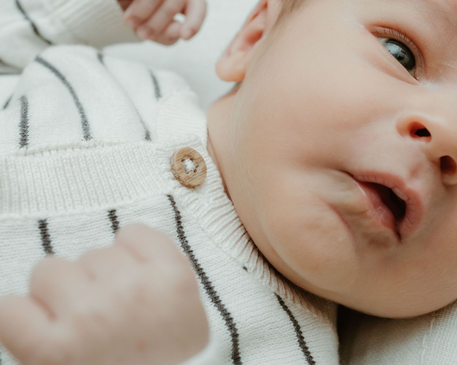 Close-up of a newborn baby in a white striped knit outfit, looking up with a curious expression.