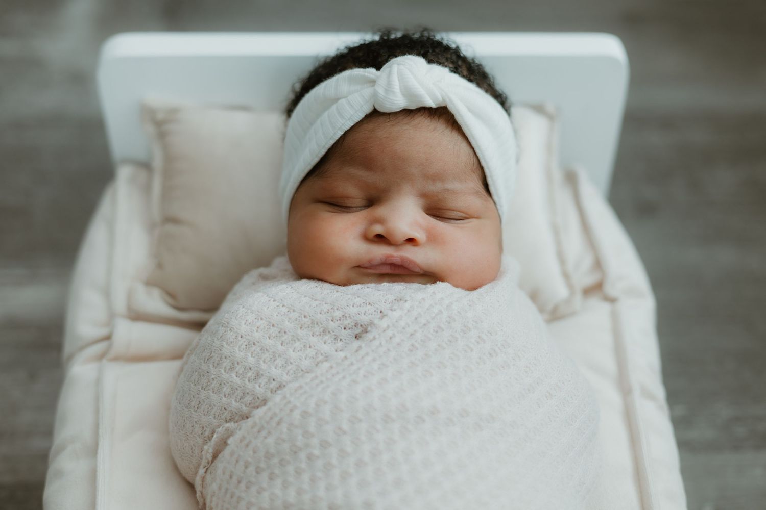 Sleeping infant wrapped in white blanket with delicate headband.