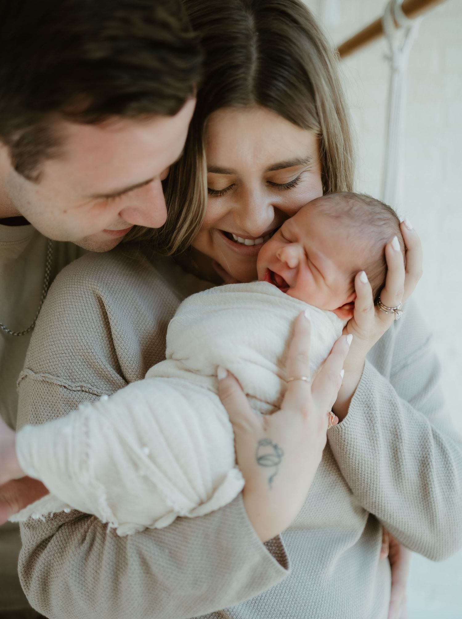 Tender family moment captured in soft grey tones as parents snuggle close with their newborn baby.
