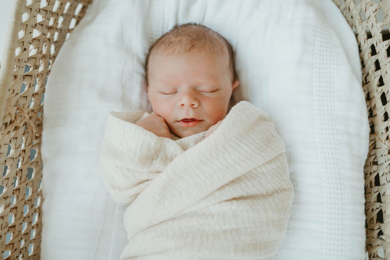 Sleeping newborn baby wrapped in cozy white knit blanket.
