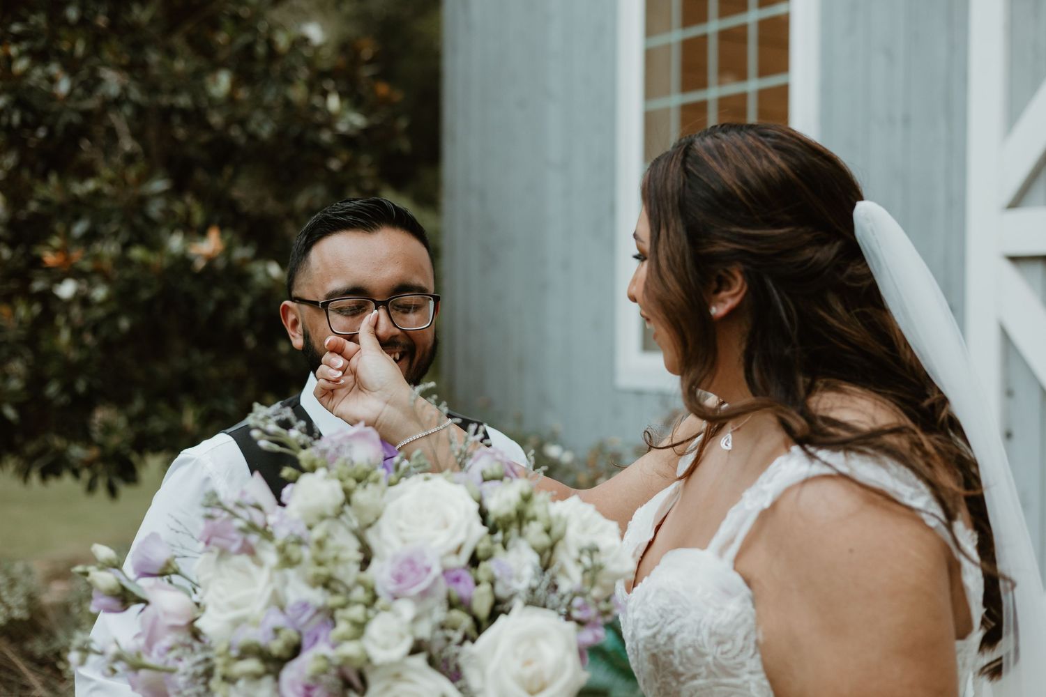 A group of wedding guests enjoy sharing a laugh at an outdoor ceremony venue surrounded by white flowers and greenery.