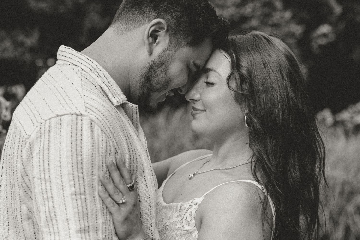 A couple shares an intimate moment during their engagement photo shoot in nature with beautiful greenery in background.