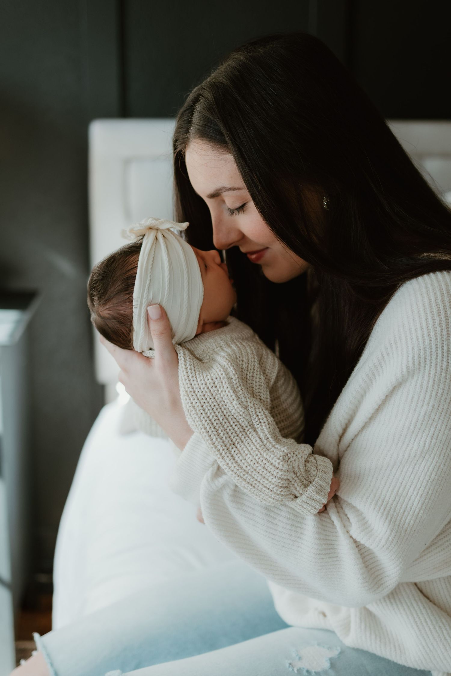 Two people in white sweaters share an intimate moment in a soft, moody lighting setting.