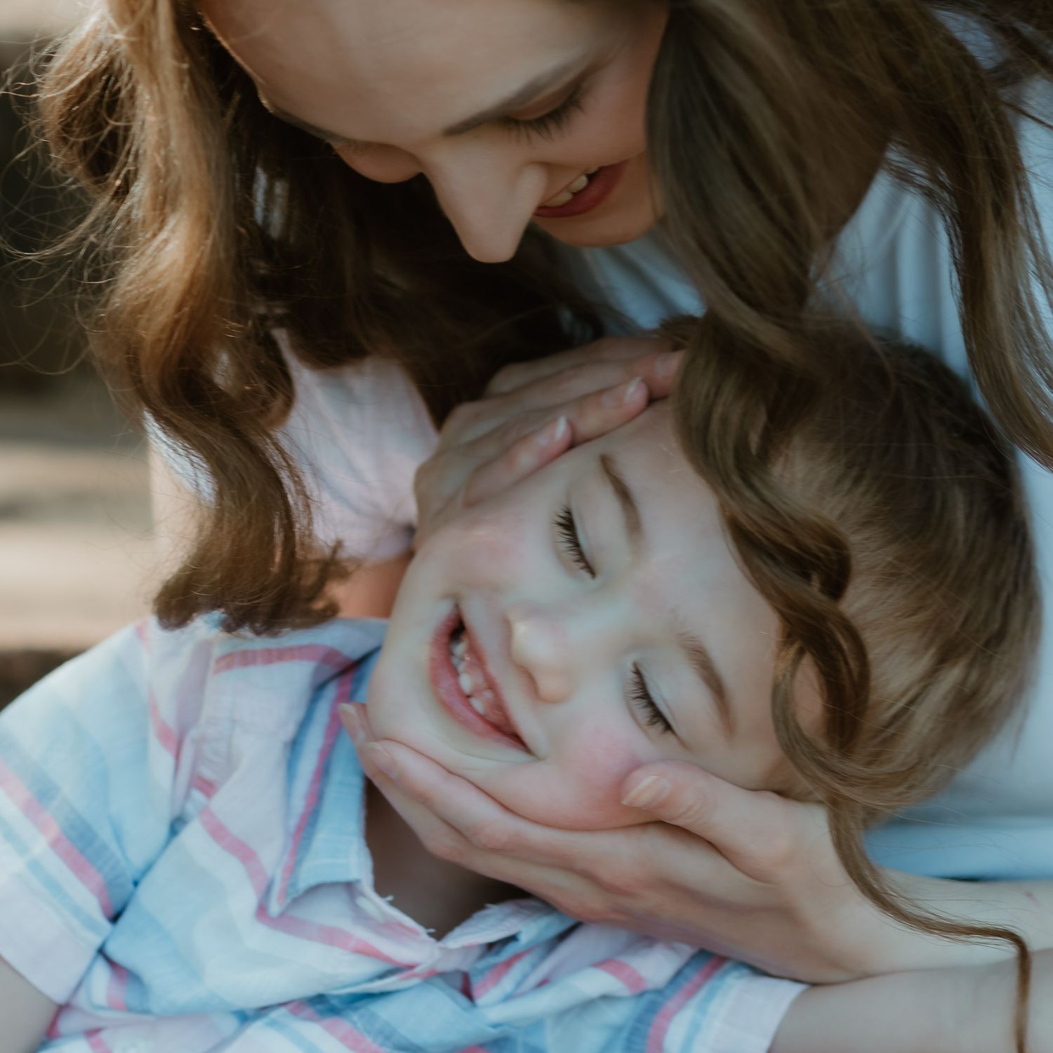 A tender moment captured between parent and child in gentle sunlight, sharing smiles and cuddles together.