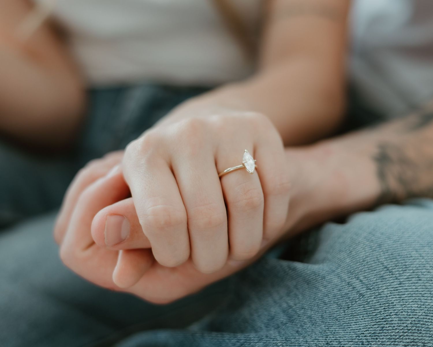 A close-up series of delicate hands with a diamond engagement ring shown from different angles on gray fabric.
