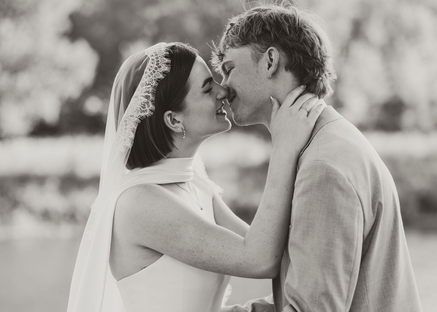 Black and white wedding photo of bride and groom sharing a romantic kiss outdoors.