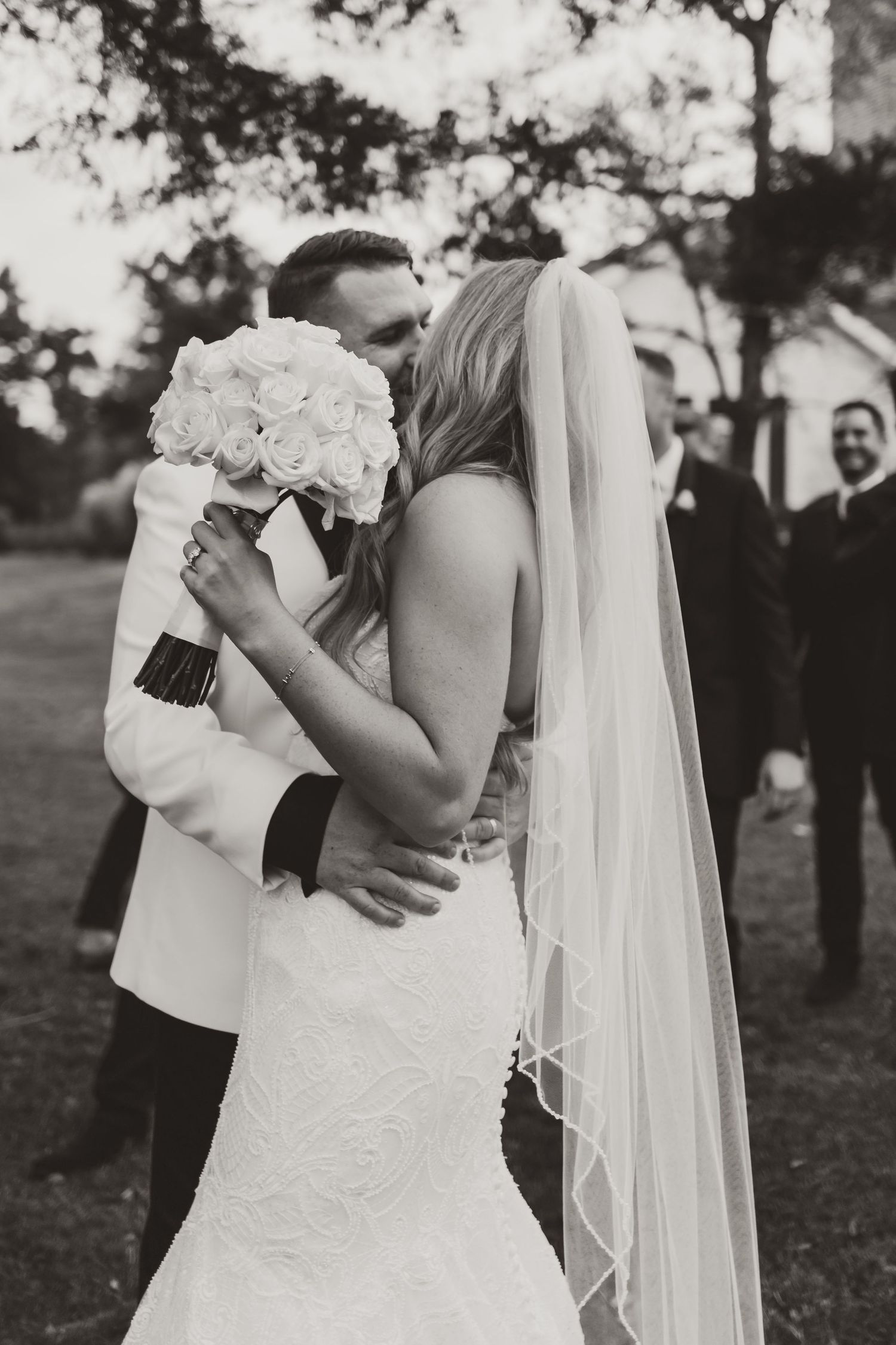 A romantic black and white wedding moment captured with a bride holding a white rose bouquet during an intimate kiss.
