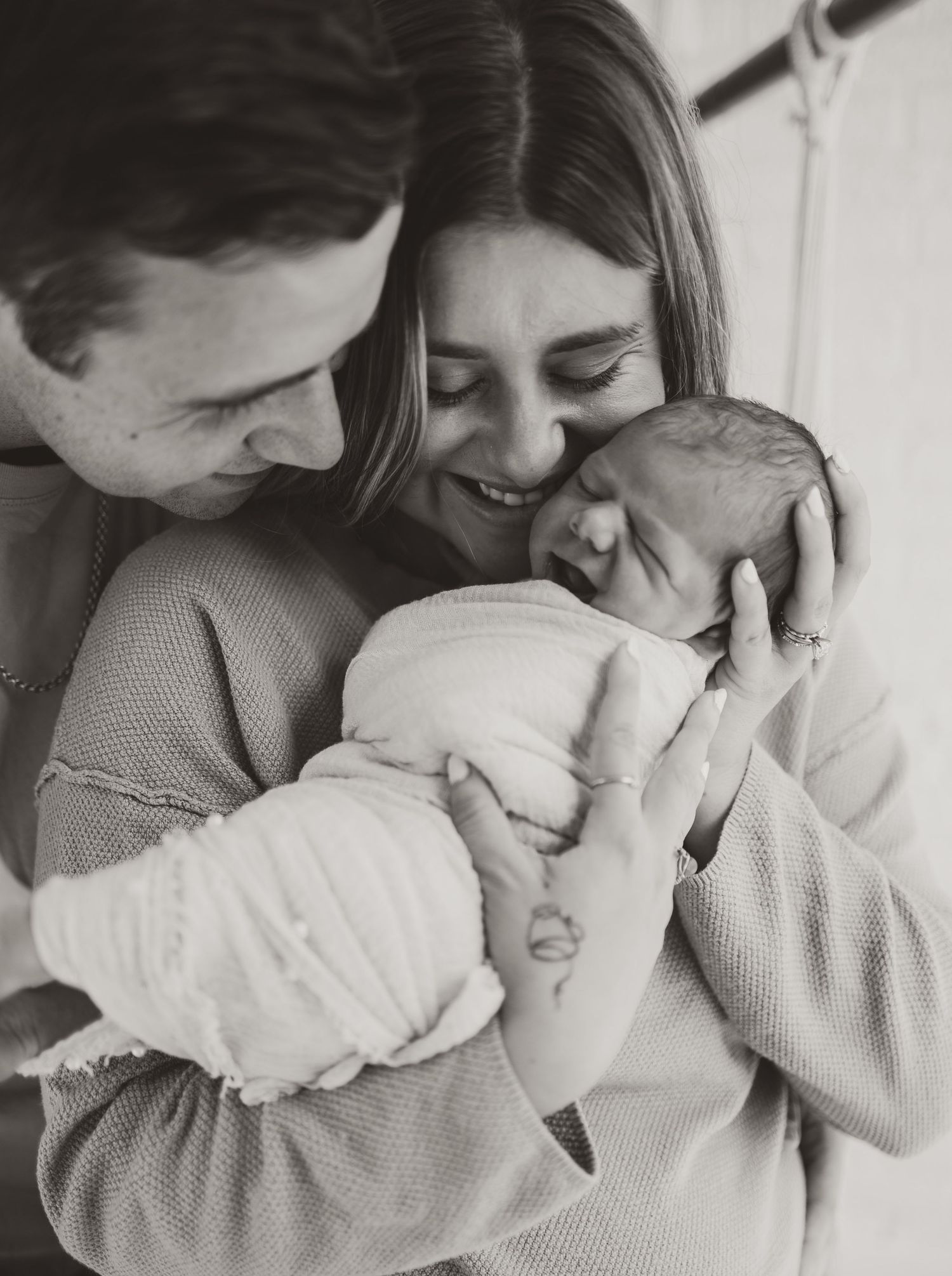A tender black and white photo series showing parents cuddling and bonding with their newborn baby.