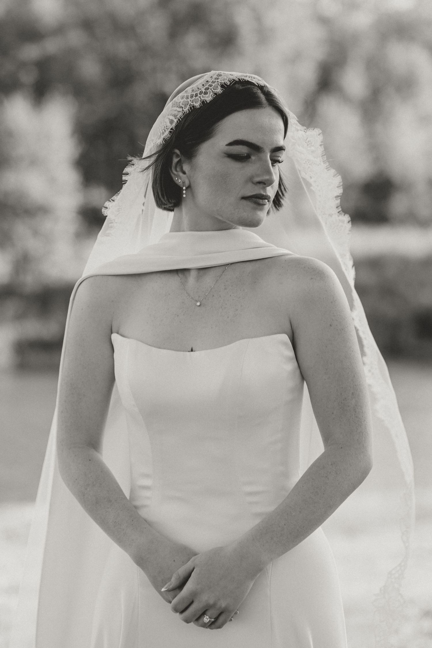 A bride in a classic white off-shoulder wedding gown poses outdoors in a series of elegant black and white portraits.