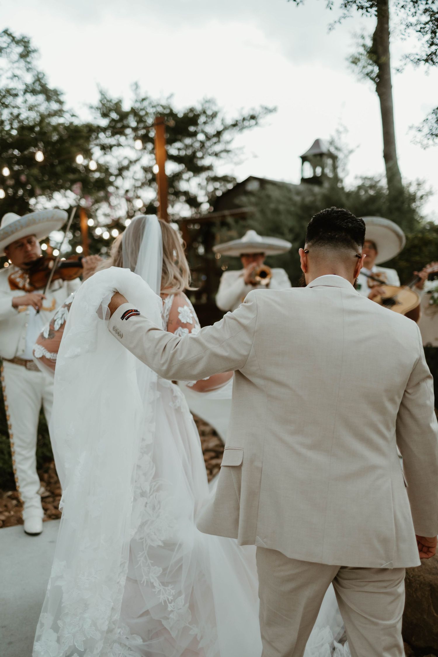 Wedding party dances in a line with the bride's white dress and groomsmen in light colored suits outdoors.