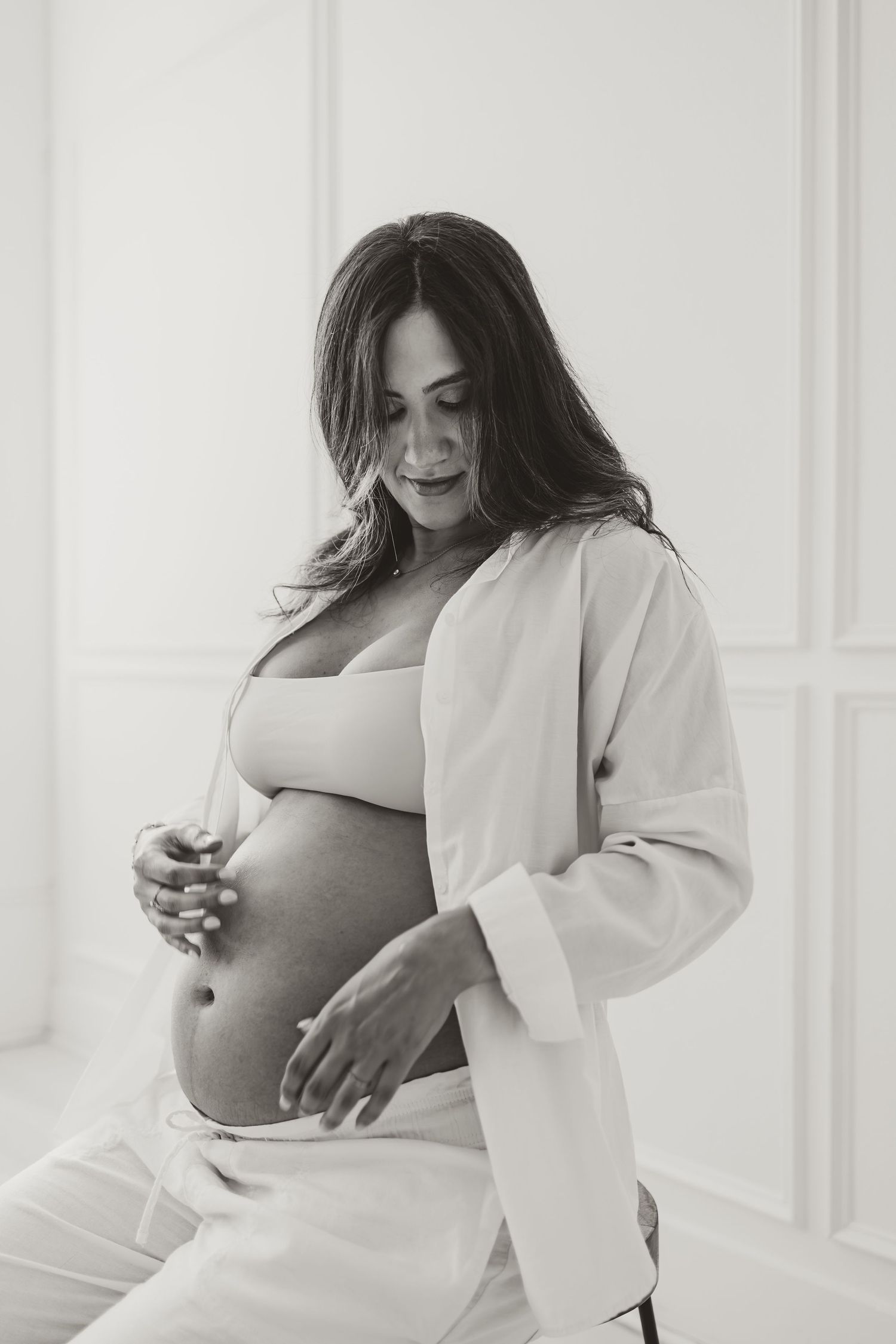 A series of intimate maternity photos showing an expectant mother in a white blazer against a light backdrop.