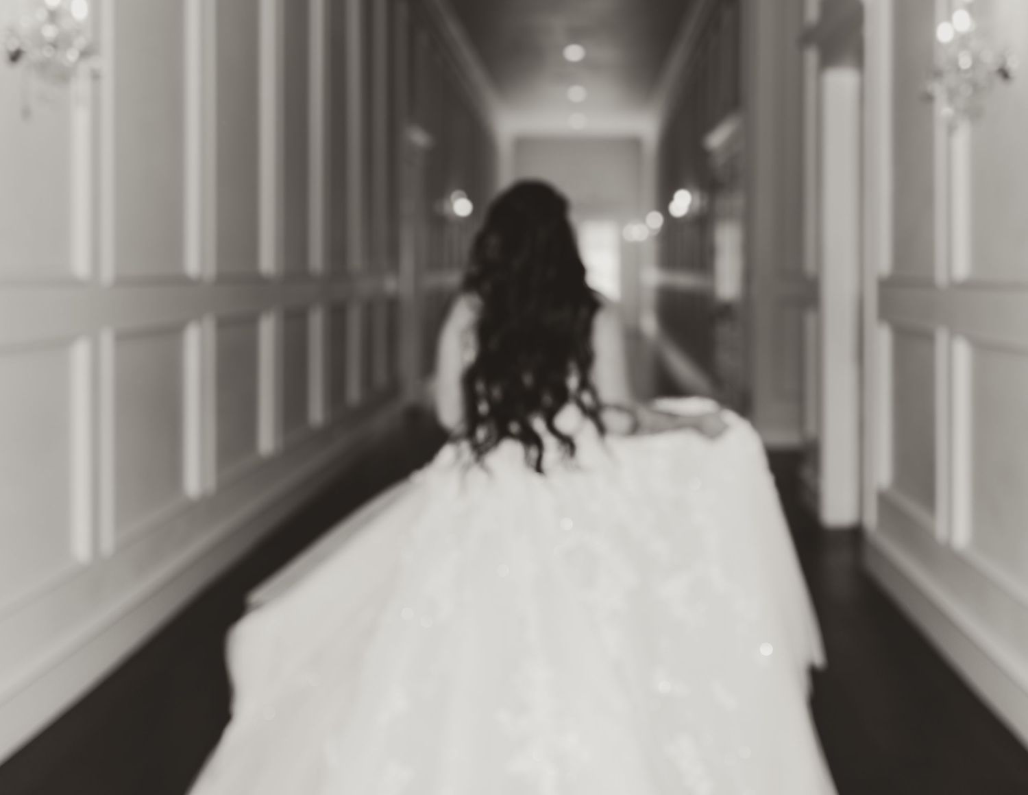 Black and white photo of a bride in a flowing wedding gown walking down an elegant hotel hallway.