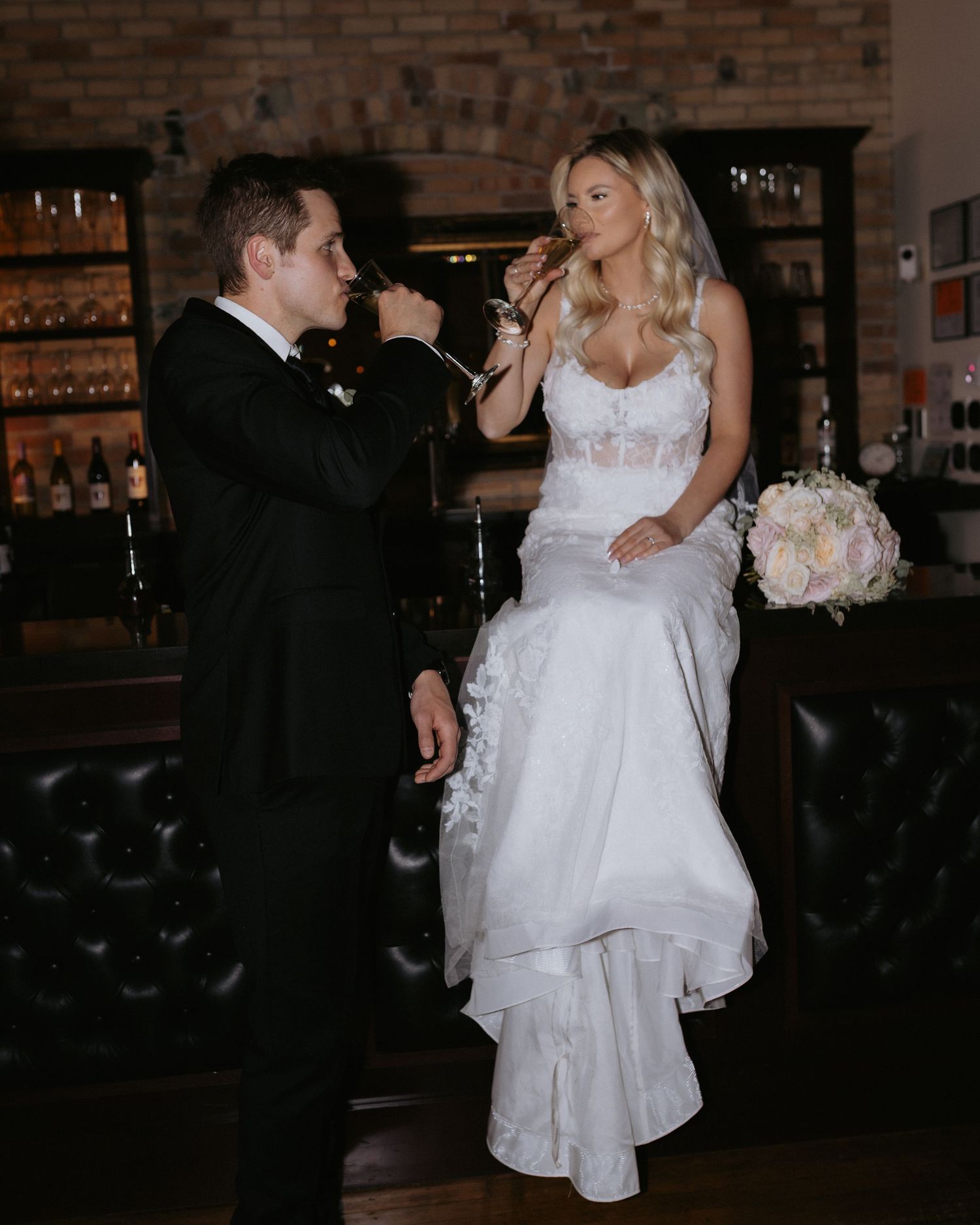 Wedding couple dancing and celebrating in a rustic venue with brick walls.