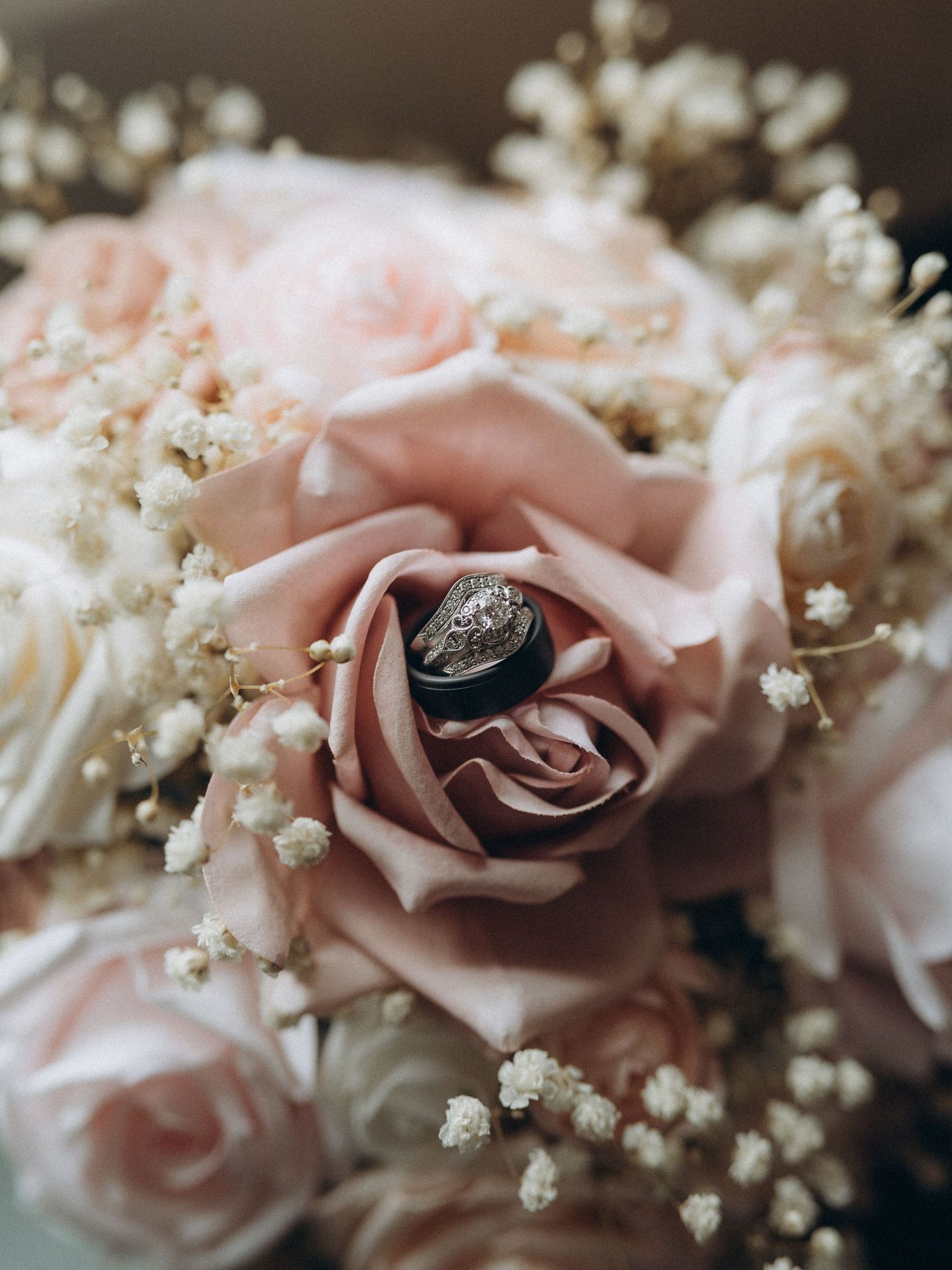 Wedding rings nestled in a blush pink rose bouquet with delicate baby's breath flowers.