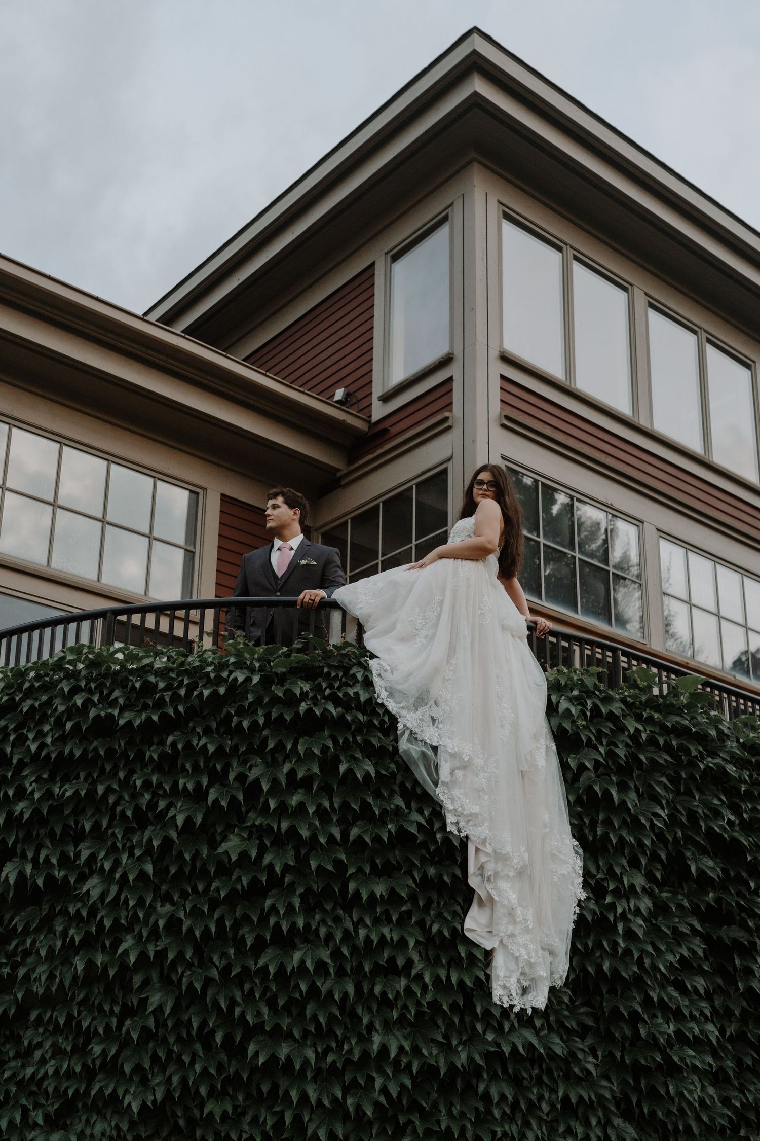 Architectural shot of a modern building with ivy-covered walls and white trim details.  With a bride and groom