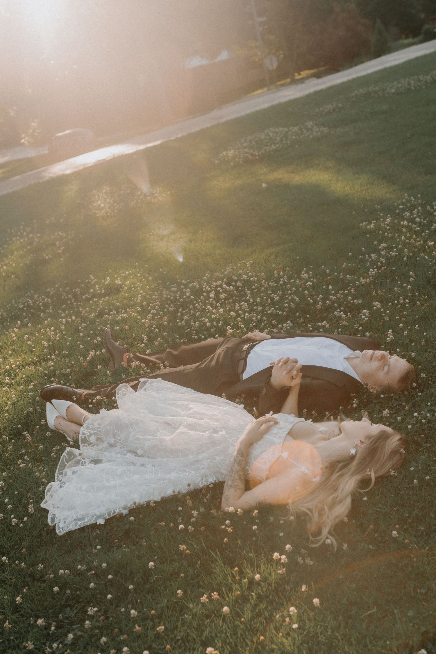 A figure in a flowing white dress lies gracefully in a sunlit meadow among wildflowers during golden hour.