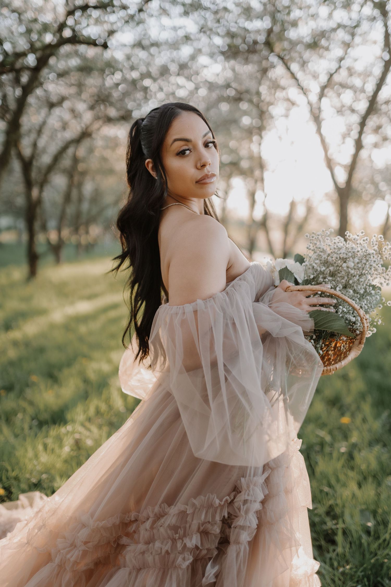 A soft pink tulle dress flows elegantly in a spring orchard setting.