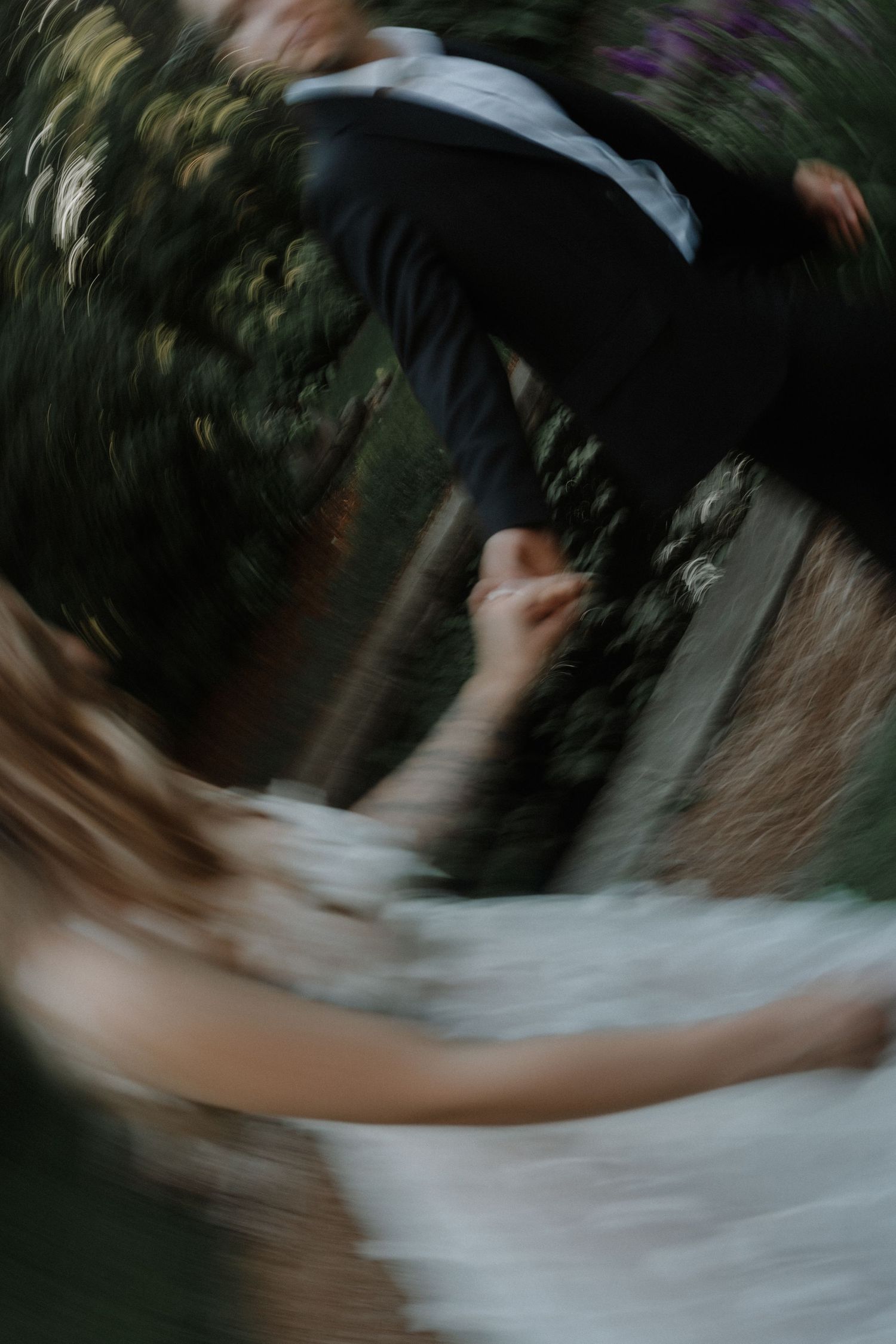 Motion-blurred artistic wedding photography captures spinning dancers in an outdoor setting.