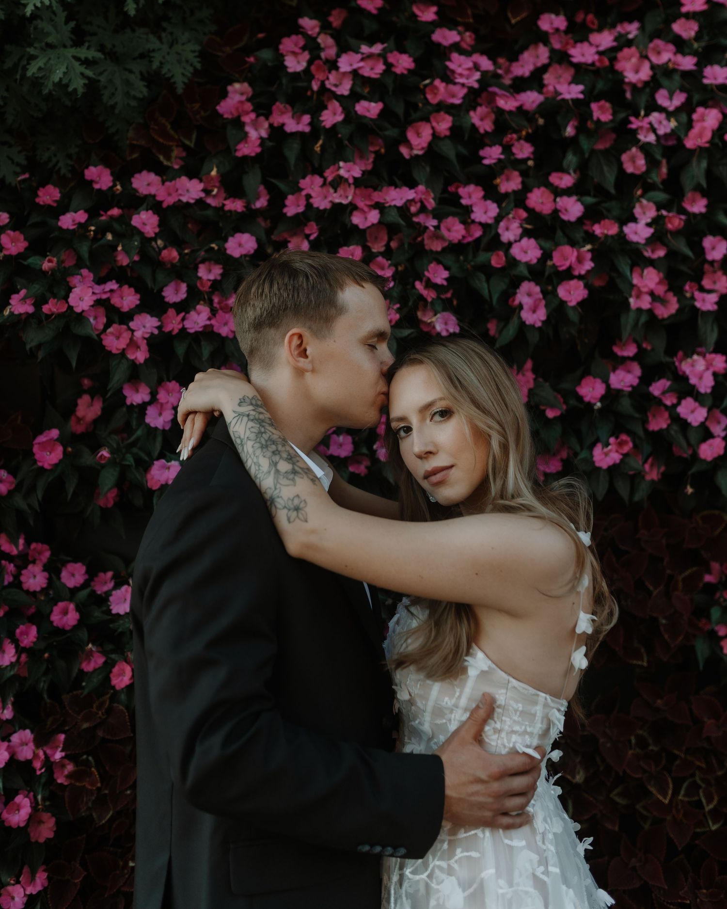 A romantic wedding couple embraces against a backdrop of vibrant pink flowering branches.
