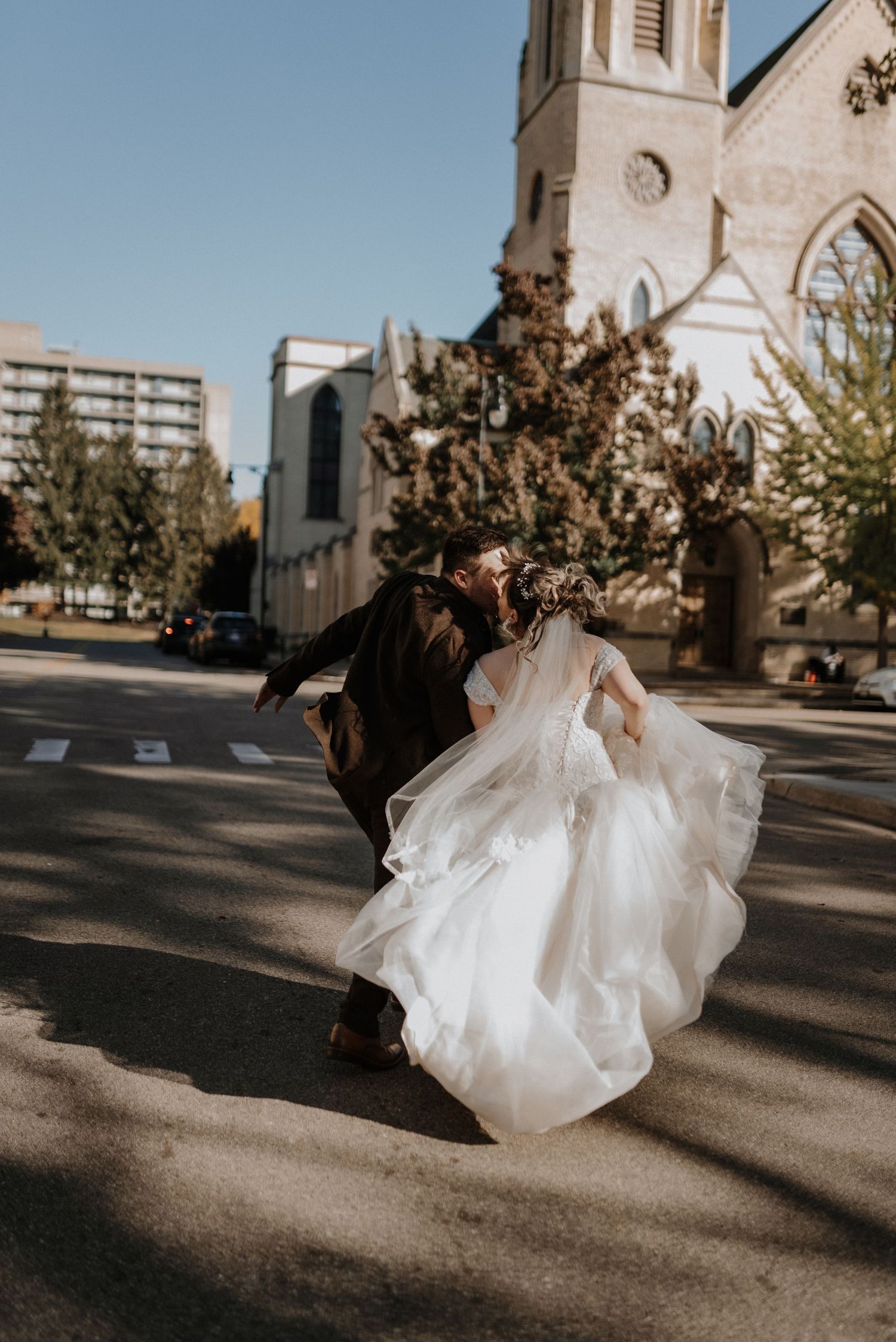 Movement of a white wedding dress twirling on a sunny day outside a church creates flowing shadows on the pavement.