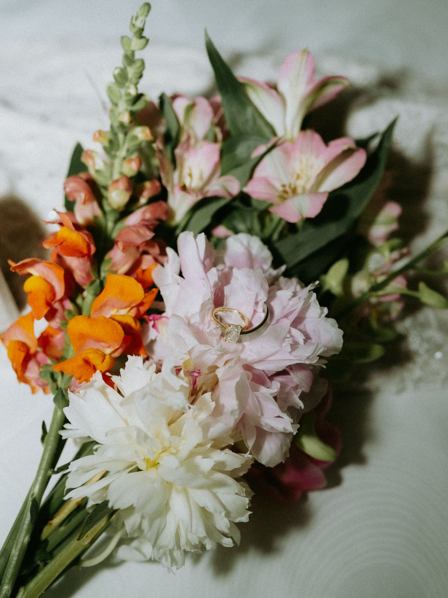 Colorful wedding bouquet with pink alstroemeria, orange snapdragons, and white carnations on a marble surface.