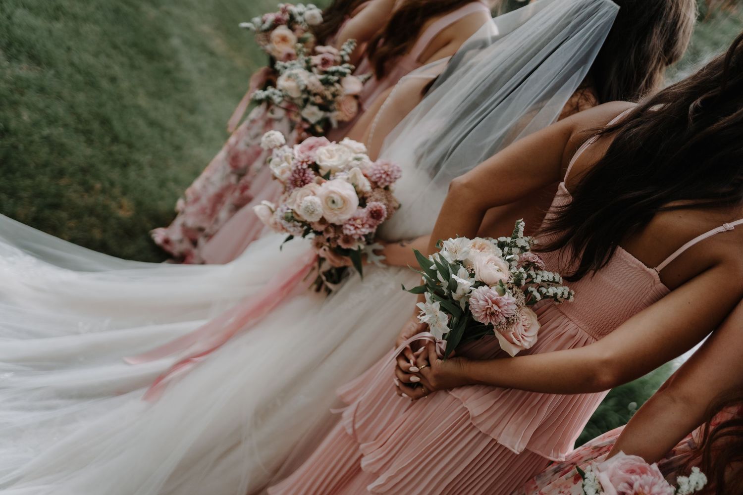 Bridesmaids dressed in blush pink dresses hold elegant pink and white floral bouquets during wedding festivities.