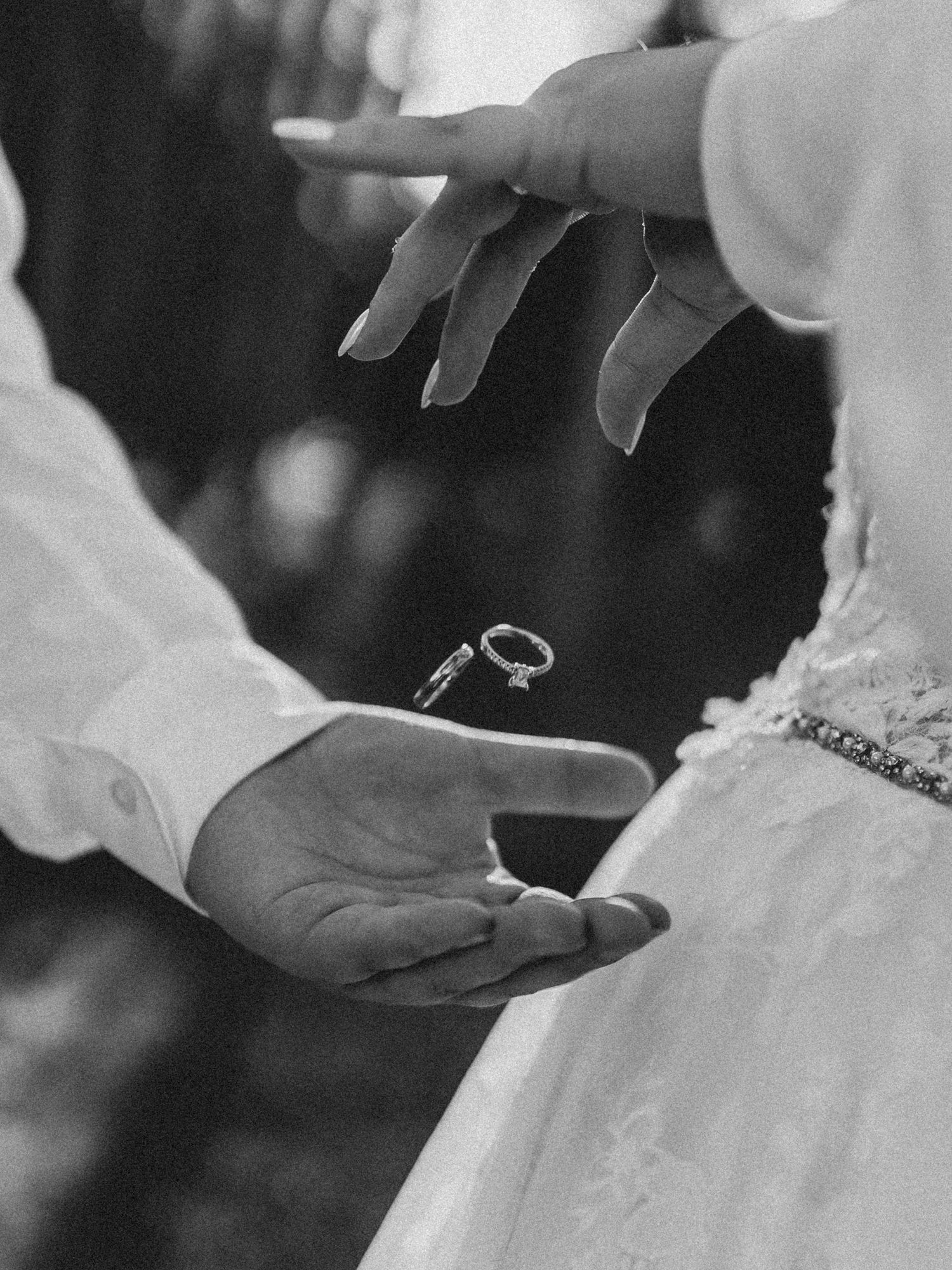 Black and white photo of a wedding ring being dropped into the groom's hand during a ceremony.