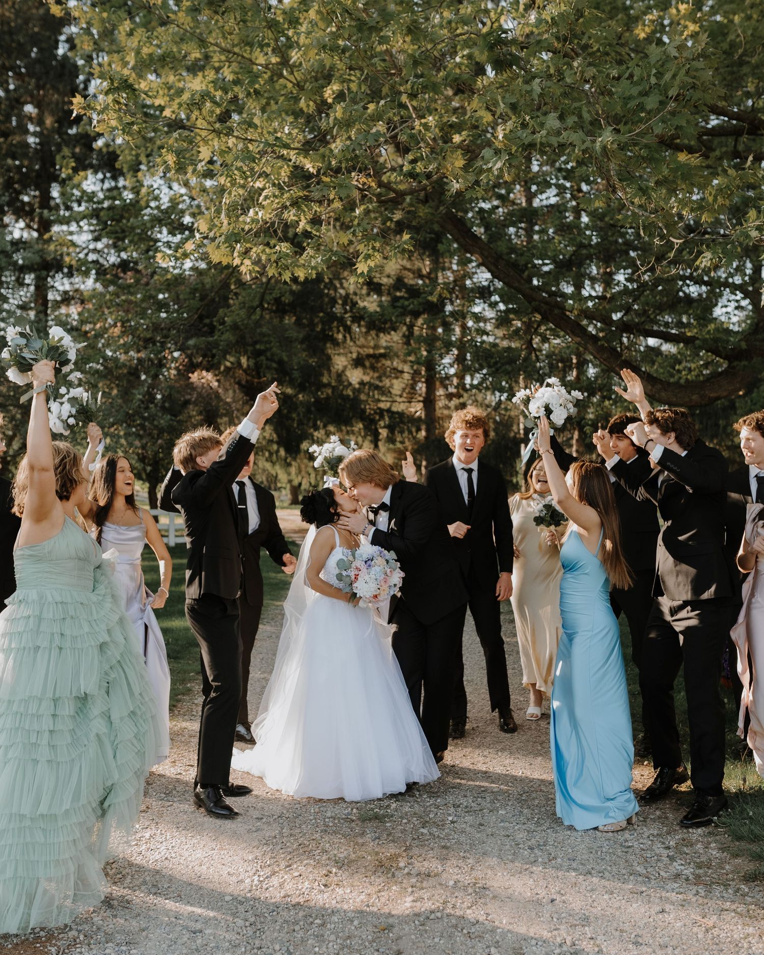Wedding party members throwing confetti during outdoor celebration under trees.
